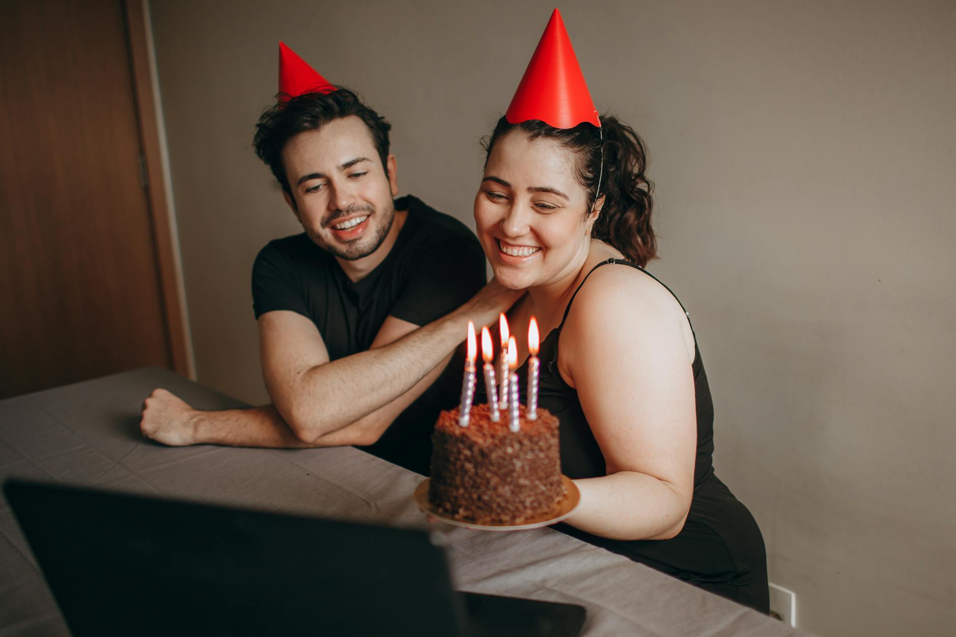 Two adults in a virtual birthday celebration with cake and hats. - long distance date ideas