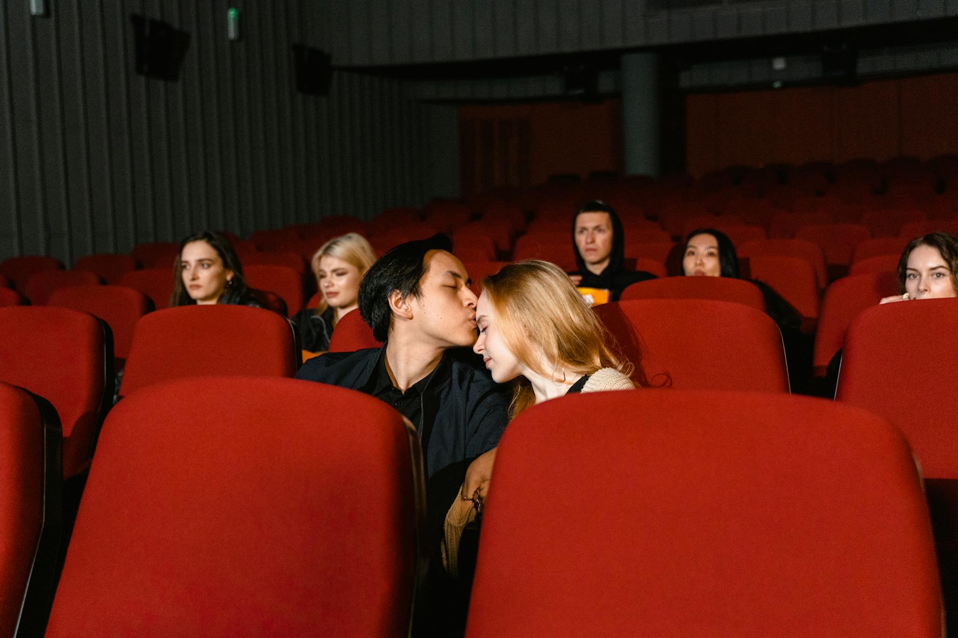 A couple shares a romantic kiss in an empty movie theater, captured from the front. - long distance date ideas