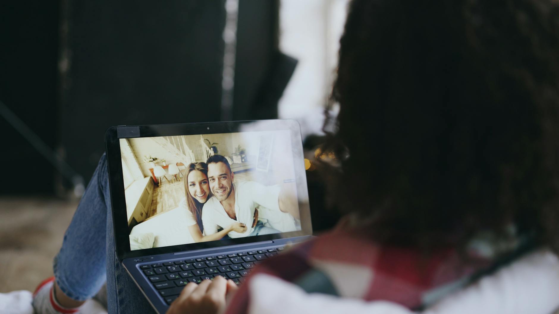 Woman viewing a happy couple's photo on a laptop at home, suggesting connection through technology. - long distance date ideas