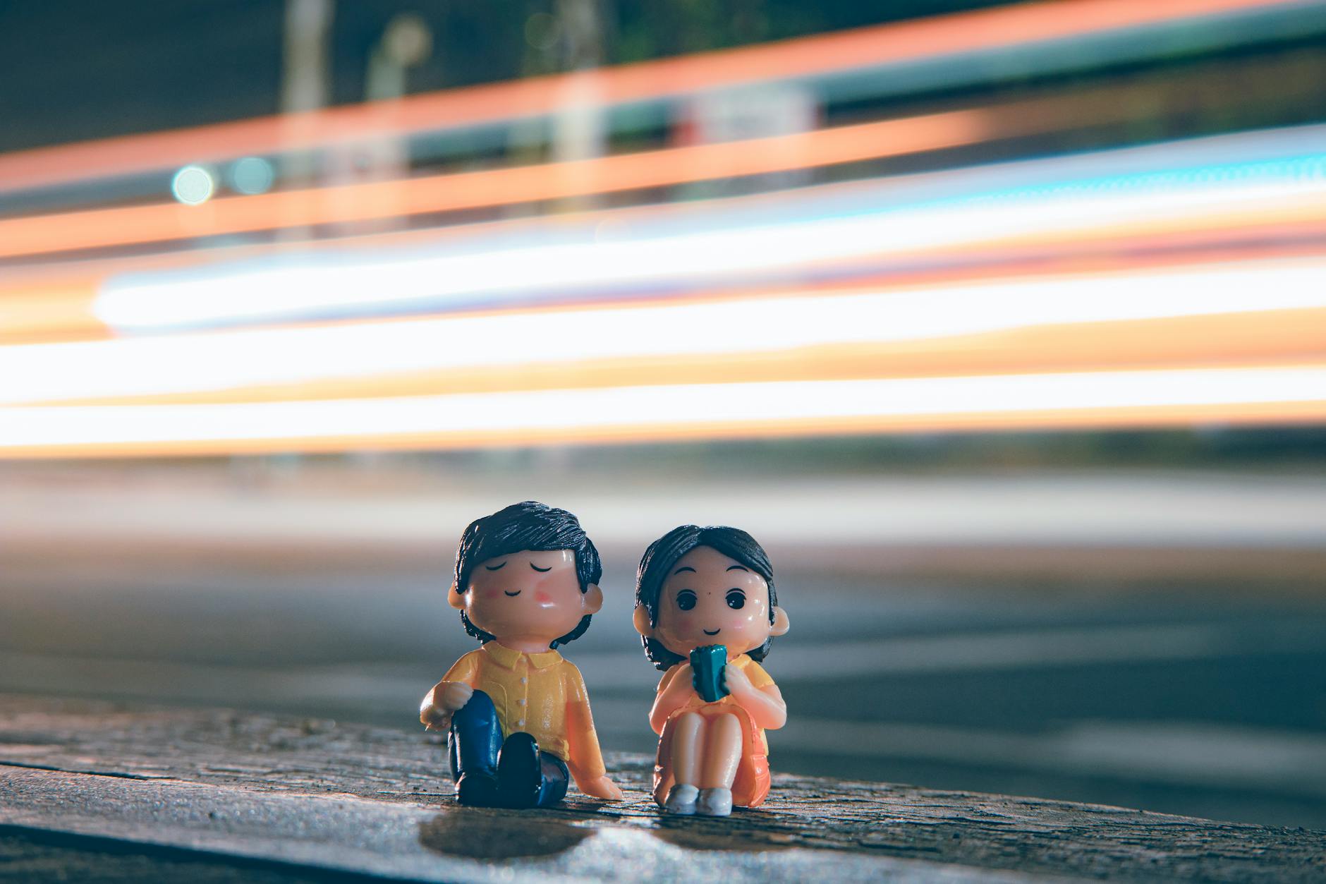 Cute figurines of boy and girl placed near asphalt road with long exposure light trails on street in evening time - long distance relationship tips