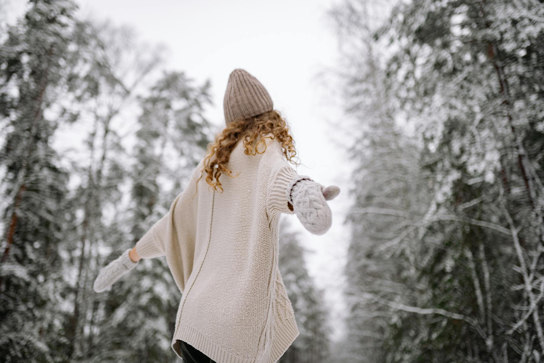 Woman in knitwear enjoying snowy forest scene in winter. Back view with arms outstretched. - manage winter anxiety