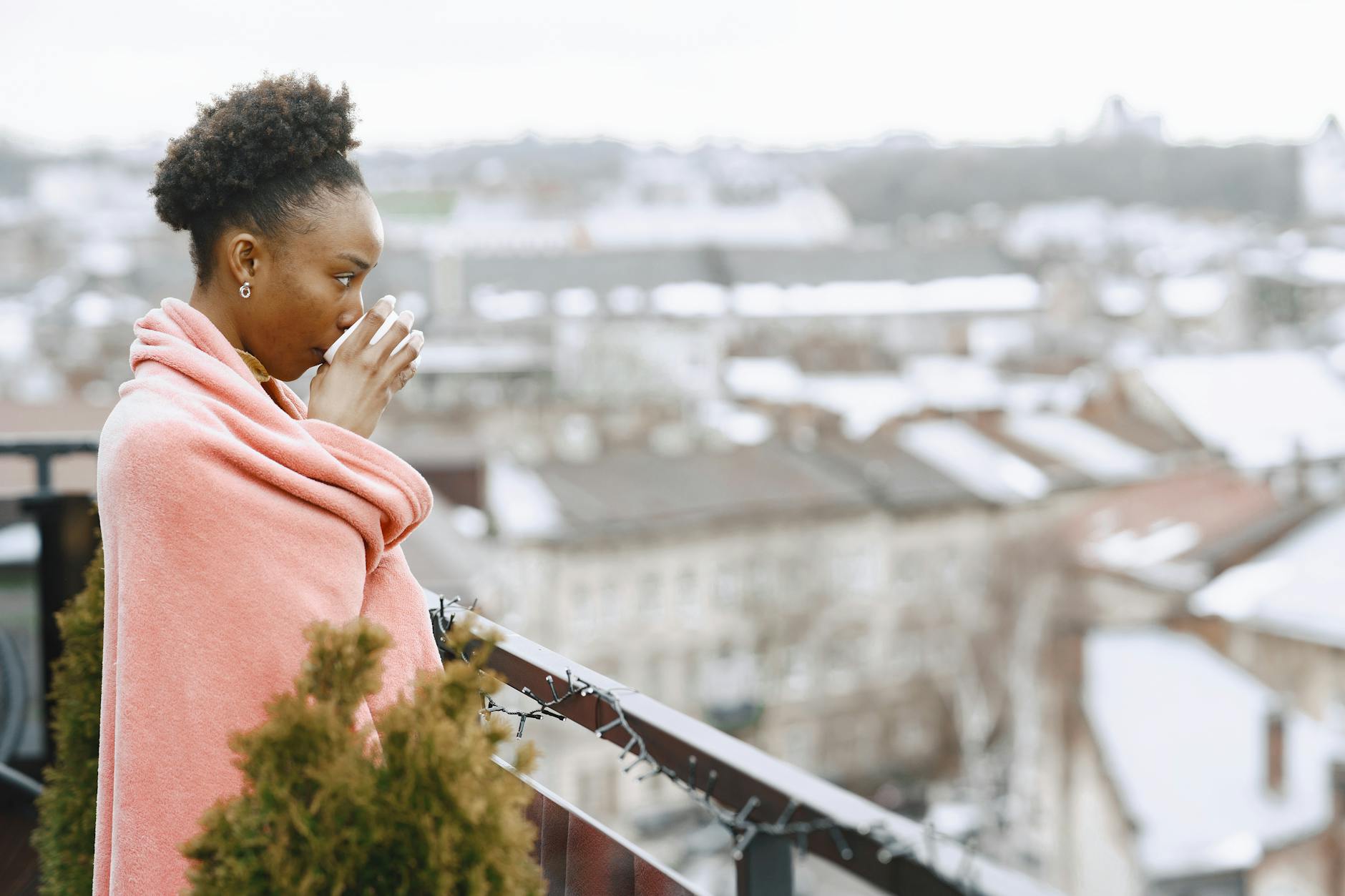A woman wrapped in a blanket enjoys a hot drink on a chilly city balcony. - manage winter anxiety
