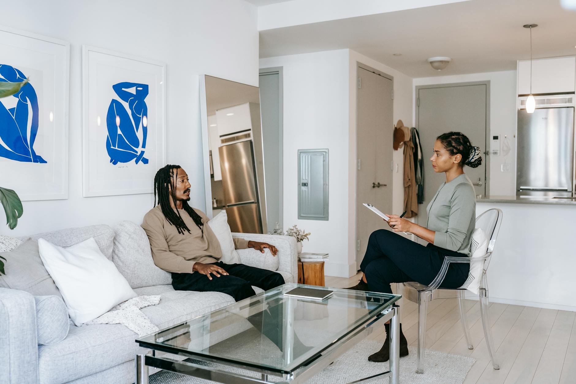 Concerned African American male in smart casual clothes sitting on comfortable sofa and sharing problems with empathetic female consultant in contemporary psychotherapy center - marriage counselor questions