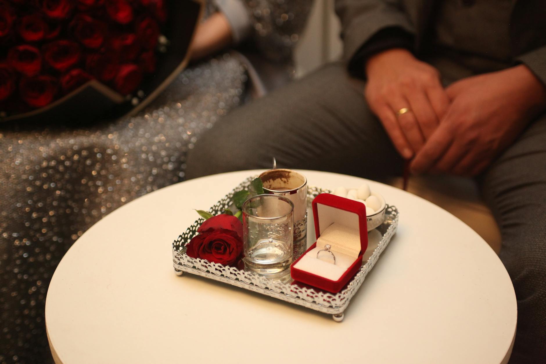 Elegant proposal setup with engagement ring and red rose bouquet on a table. - marriage plateau