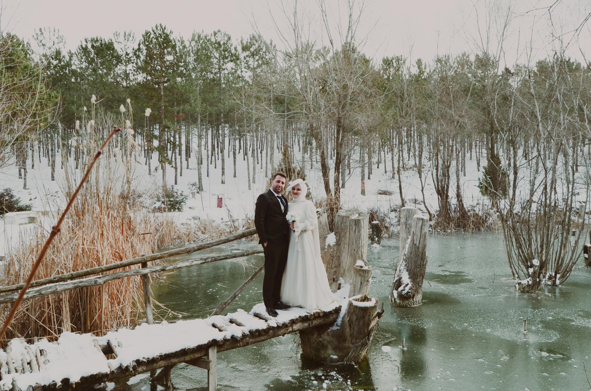 Bride and groom stand on a snow-covered bridge in a serene winter landscape. - marriage after winter