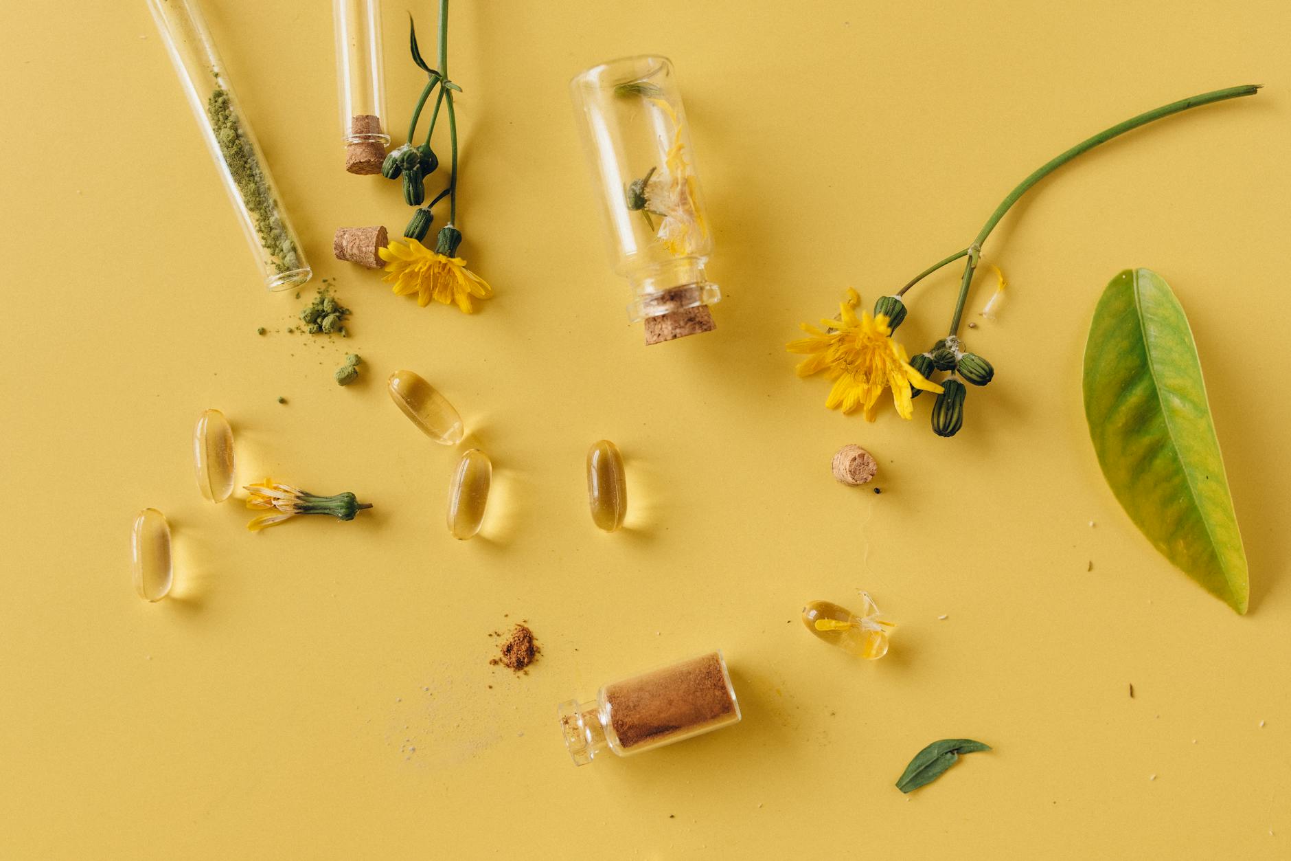 A flat lay of glass bottles, capsules, and flowers on a vibrant yellow surface, representing natural remedies. - natural mood boosters