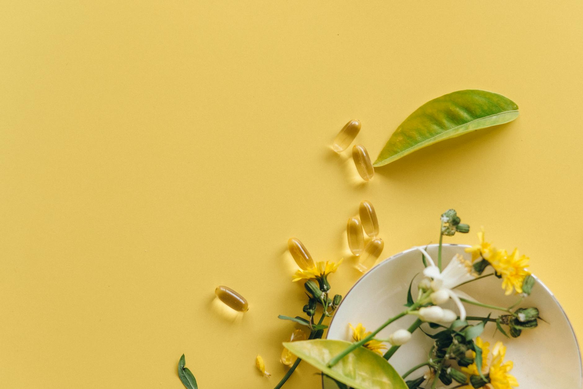 Flat lay of herbal supplements, flowers, and leaves on a bright yellow background. - natural mood boosters