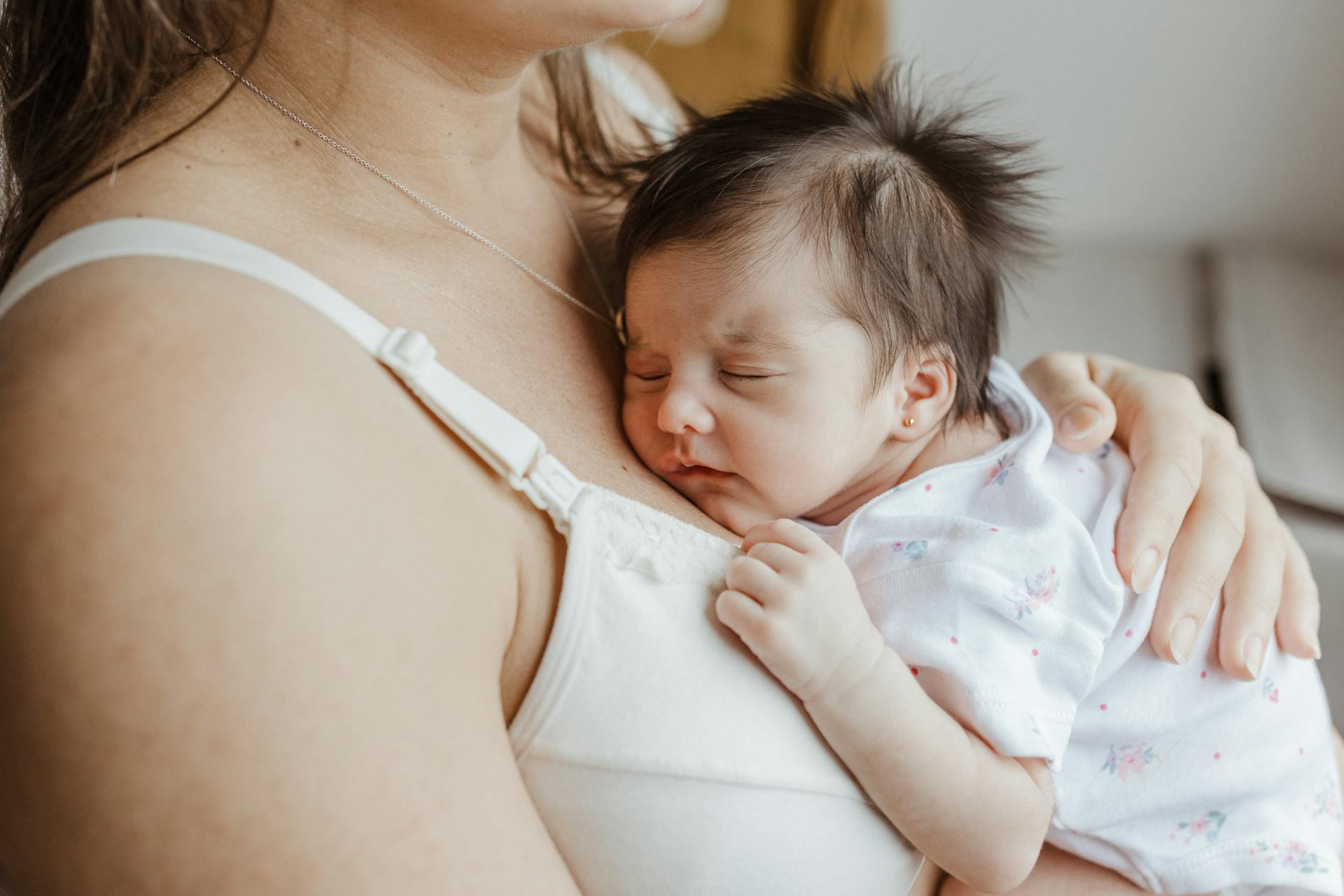 A mother holds her sleeping newborn close, showcasing love and bonding indoors. - new parent sleep
