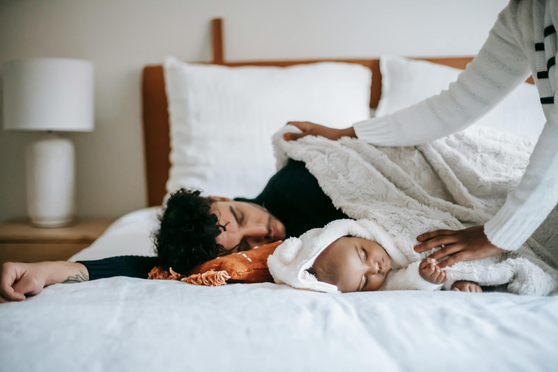 Crop faceless black woman in casual clothes spreading blanket on diverse husband and baby sleeping together on soft bed in morning - new parent sleep