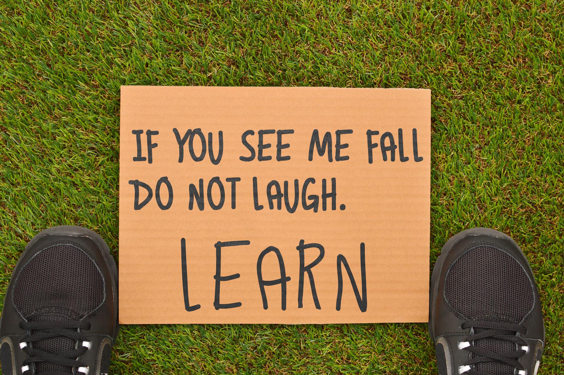 Cardboard sign with motivational message beside sneakers on green grass. - overcome perfectionism