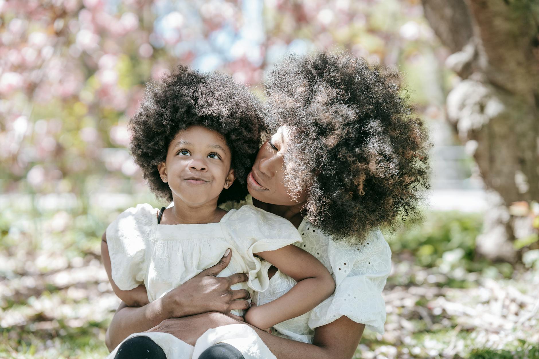 A mother and daughter with afro hair enjoy a moment together outdoors under cherry blossoms. - parent burnout spring