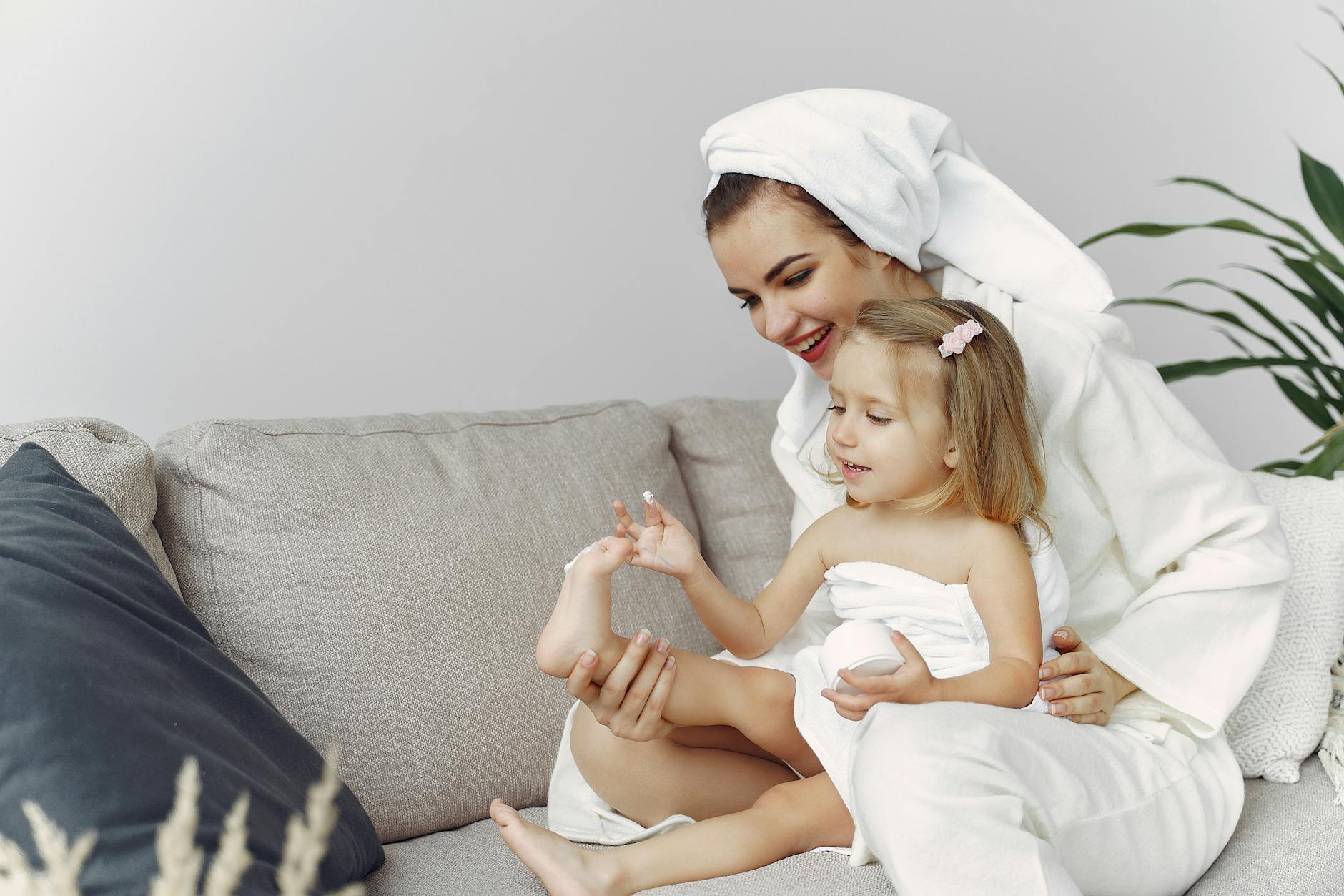 A mother and daughter enjoy bonding time on the sofa, wrapped in towels. - parental burnout self care