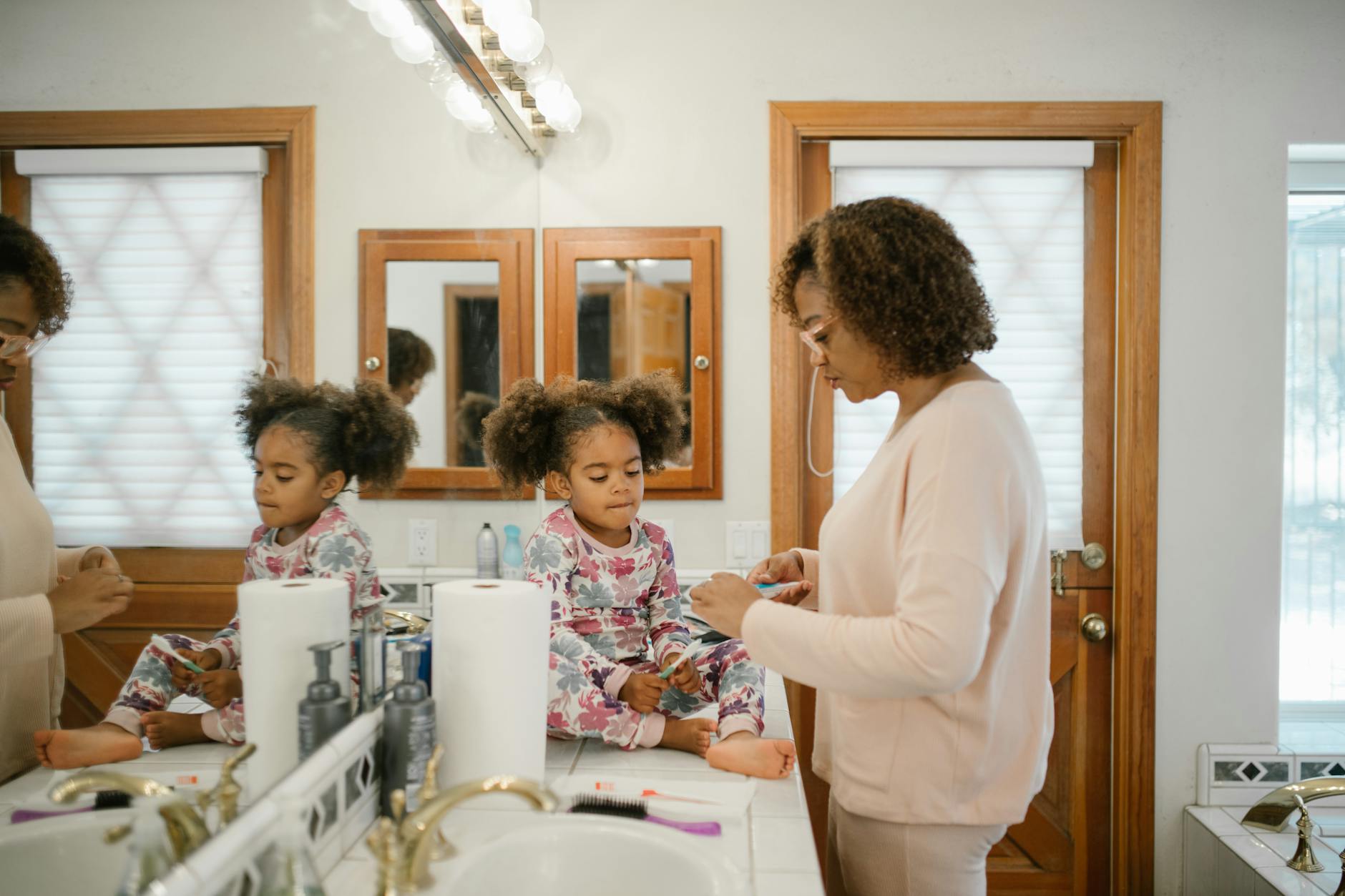 A mother assists her young daughter with her morning routine in a bright bathroom setting. - parental burnout self care