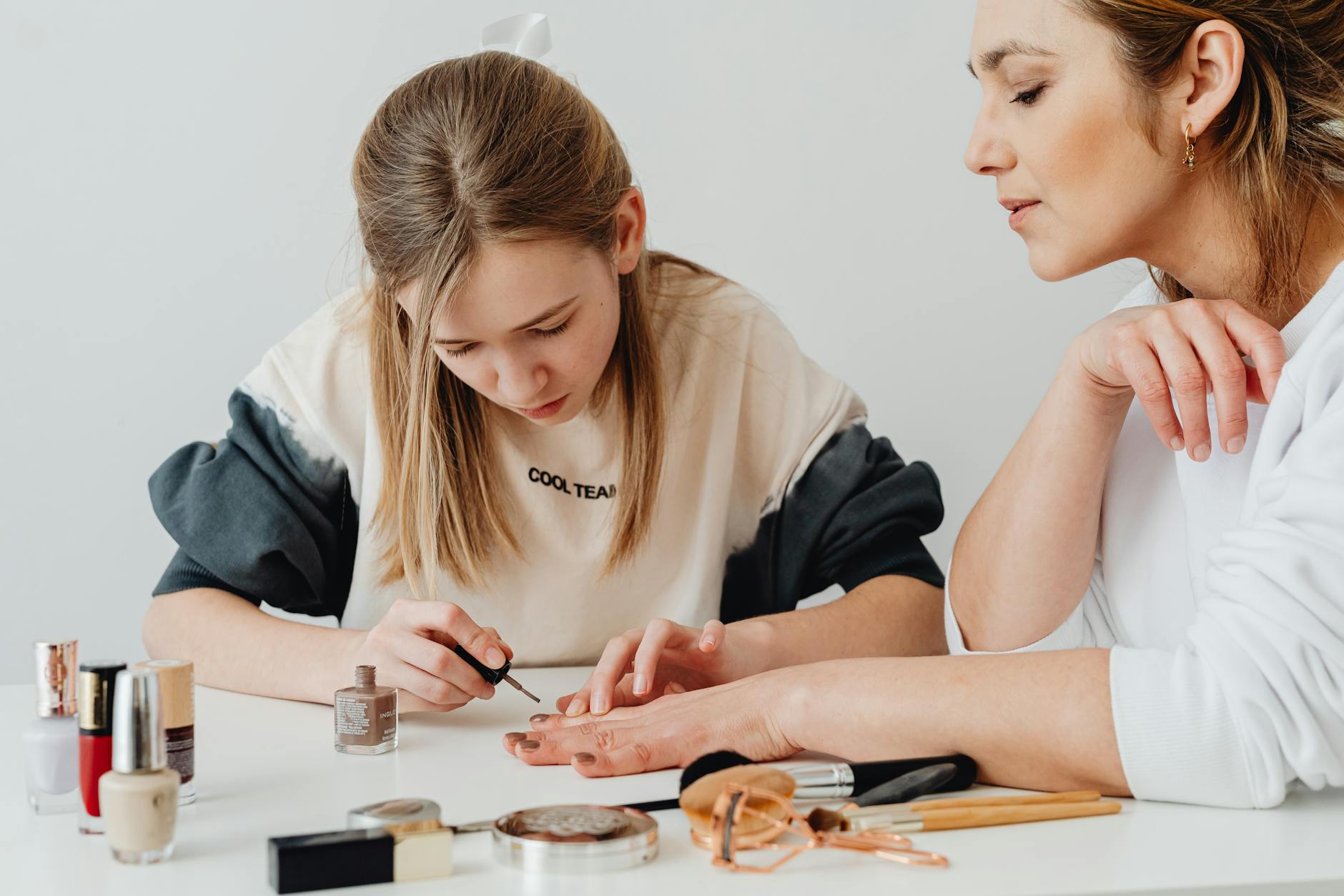 A mother and daughter enjoy quality time painting nails indoors, surrounded by cosmetics. - parental burnout self care