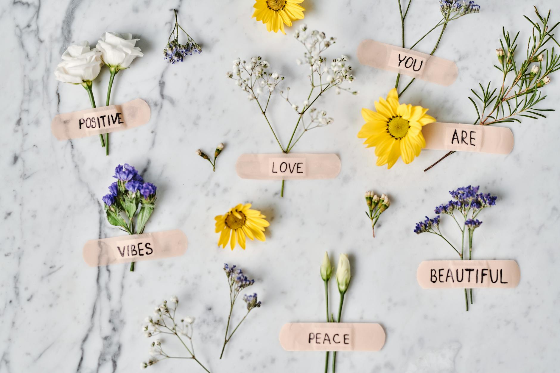 Floral flat lay with positive words on band-aids over a marble surface, promoting peace and love. - post breakup healing