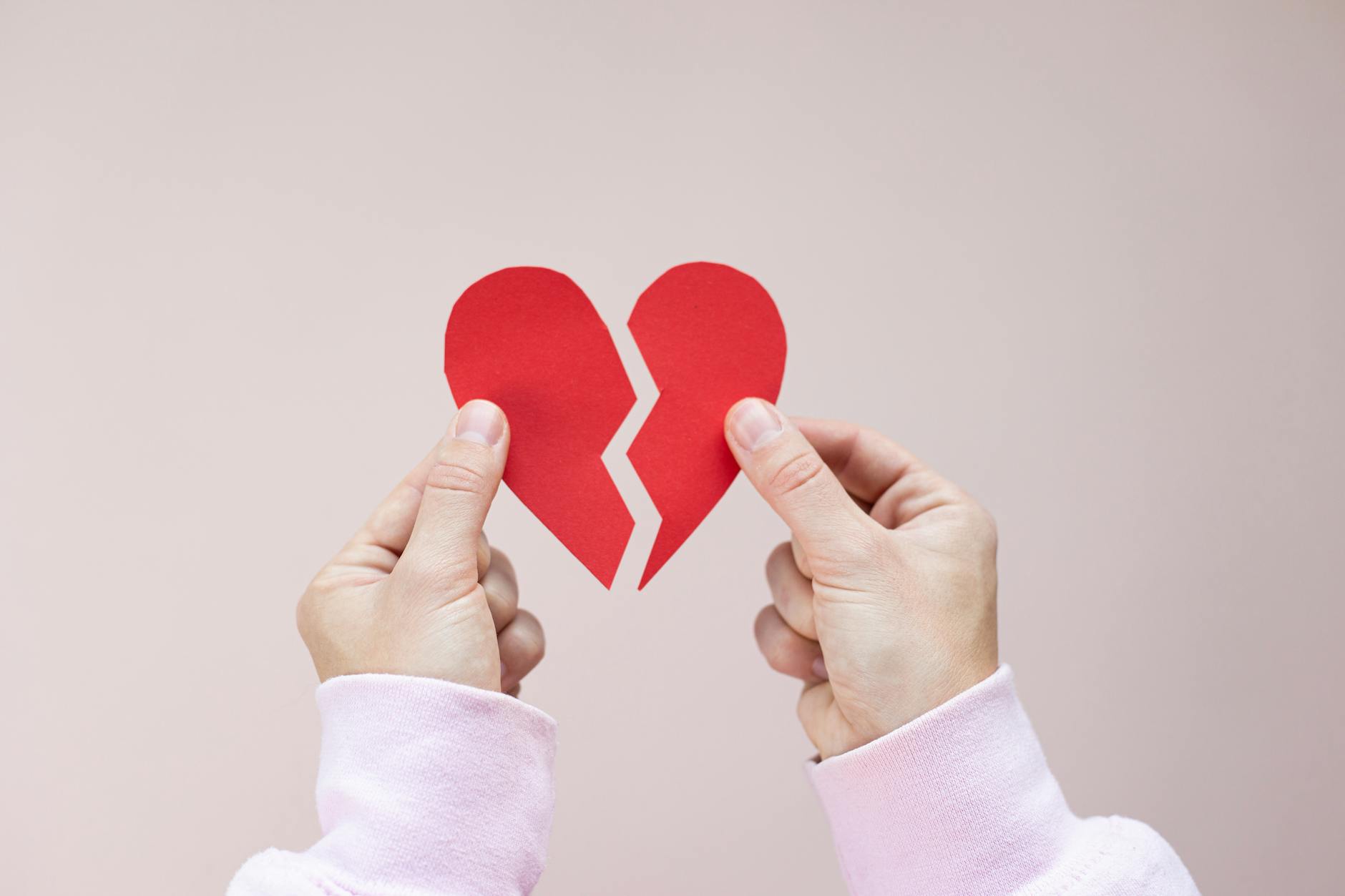 Crop unrecognizable person demonstrating red handmade parts of paper heart against white background - post breakup healing