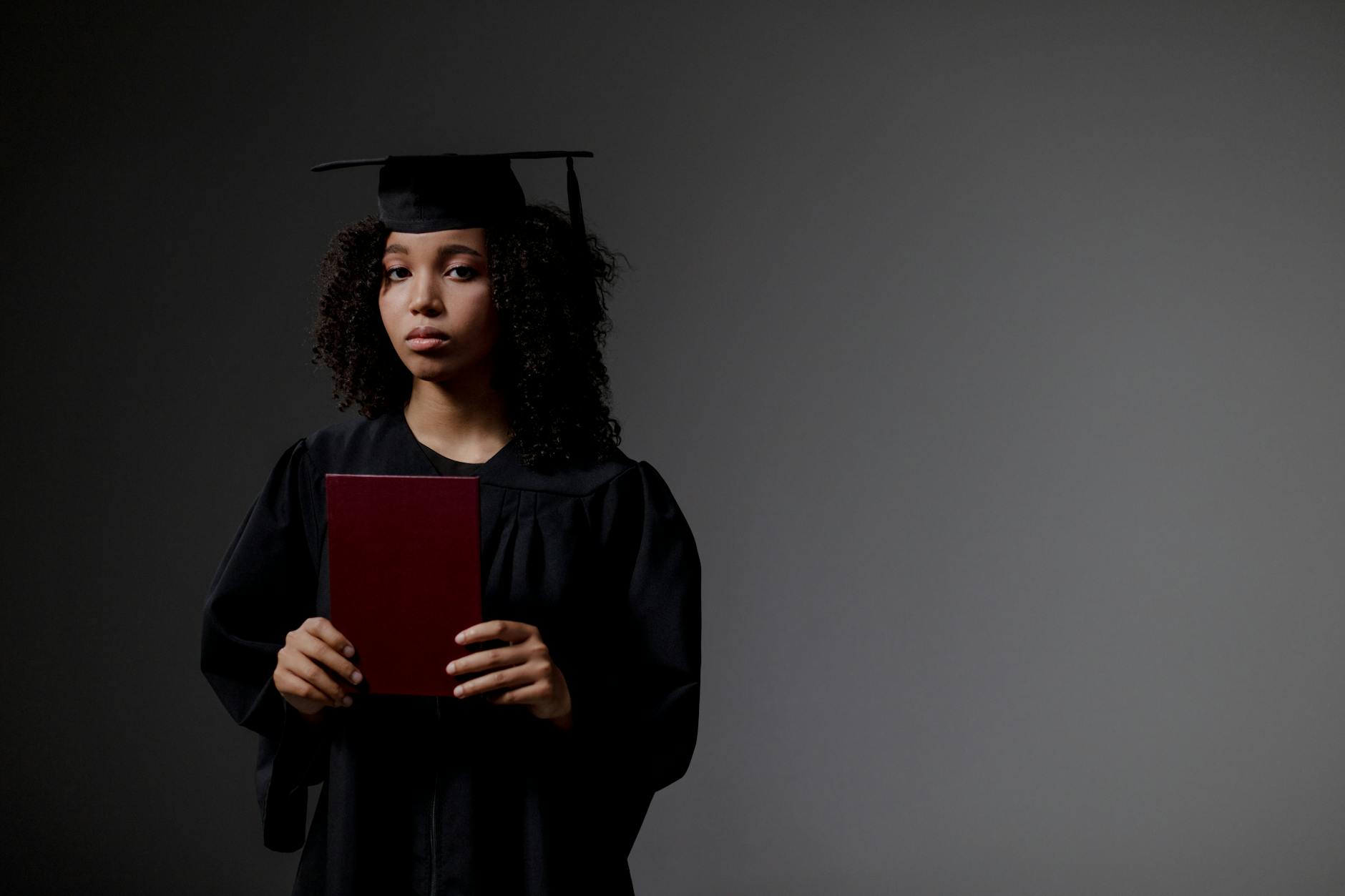 Young graduate in black academic regalia holds diploma, looking serious. - post grad adjustment