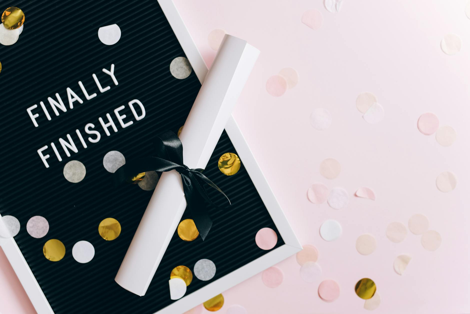 A graduation scene with a diploma and confetti on a letter board reading 'Finally Finished.' - post grad adjustment