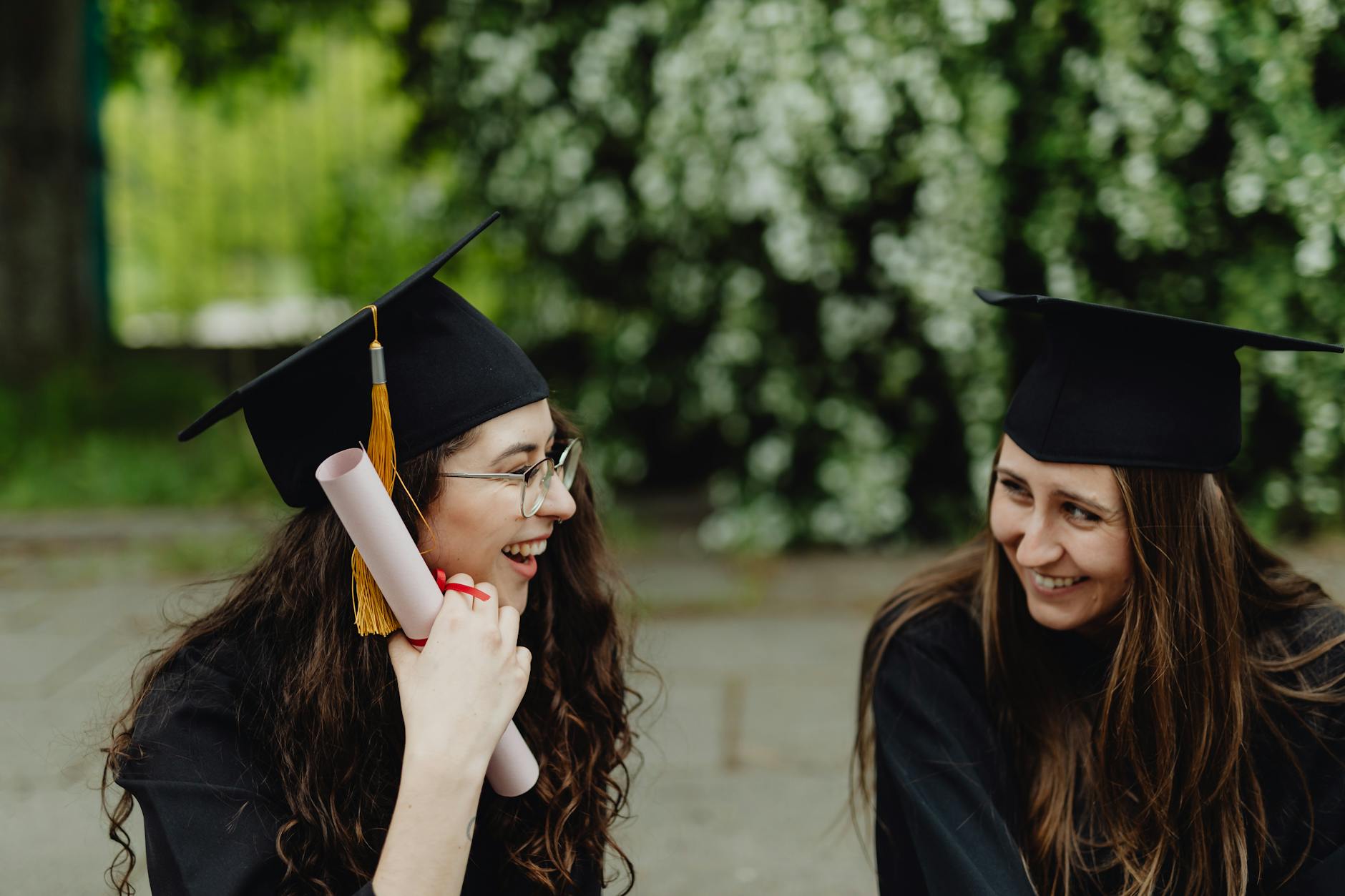 Two women celebrating their graduation with diplomas and caps outdoors. - post grad relationships