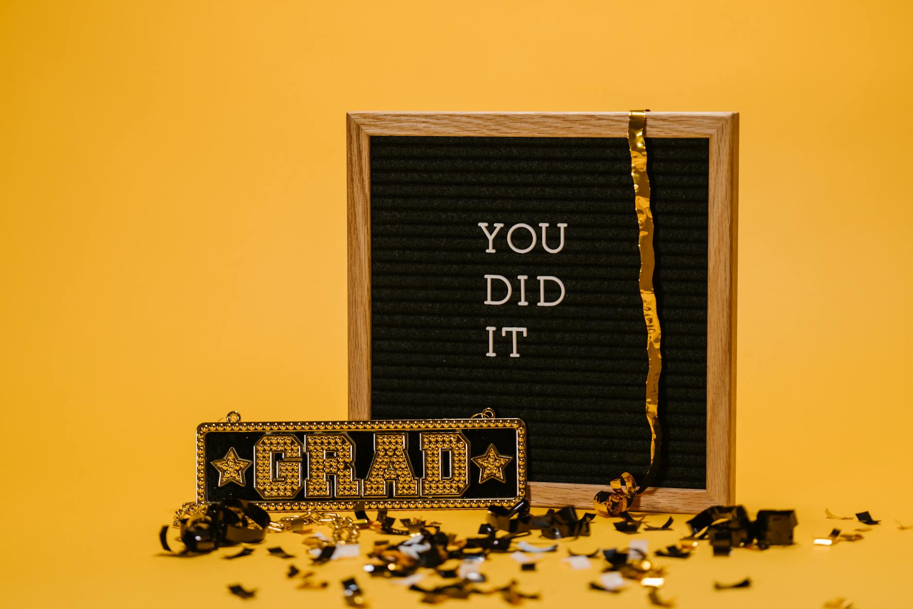 A graduation celebration with a letter board and confetti on a vibrant yellow background. - post grad resilience