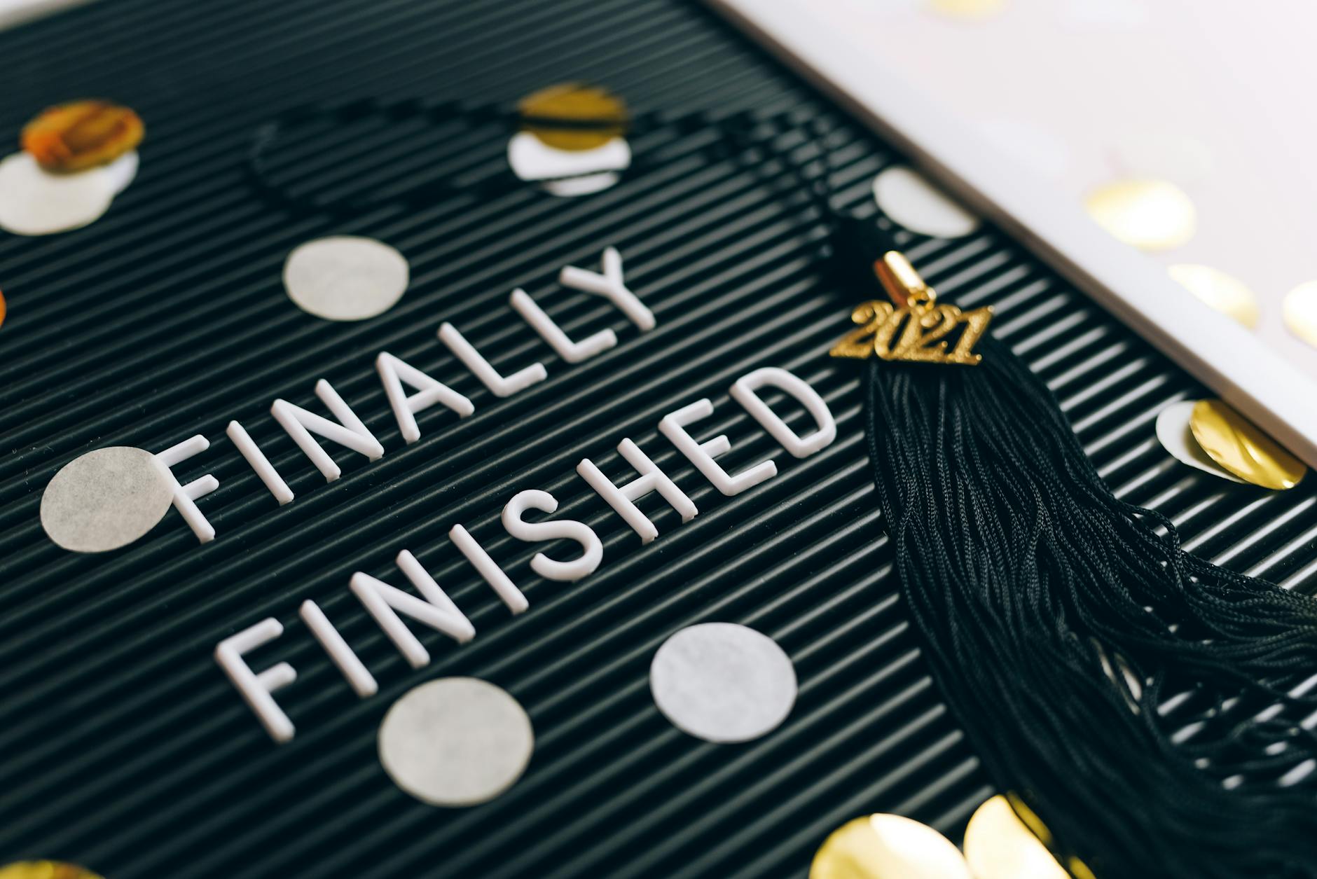 Close-up of 'Finally Finished' sign with graduation tassel and 2021 charm on letter board. - post grad resilience