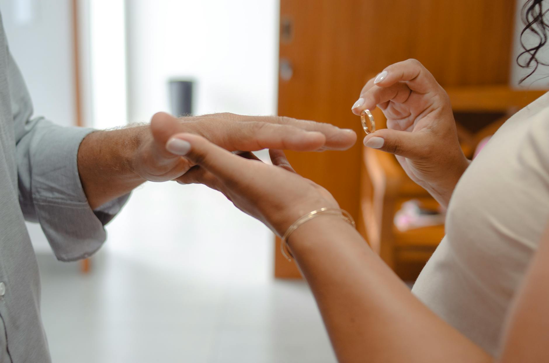 Intimate close-up of a couple's hands exchanging wedding rings indoors. - post wedding connection