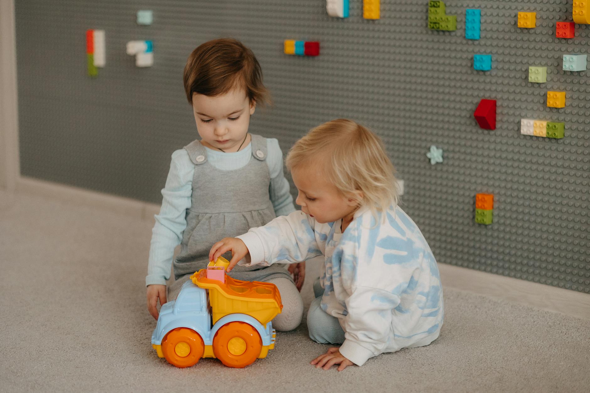 Two young children playing with a toy truck in a cozy indoor setting, exploring together. - preschool sharing activities