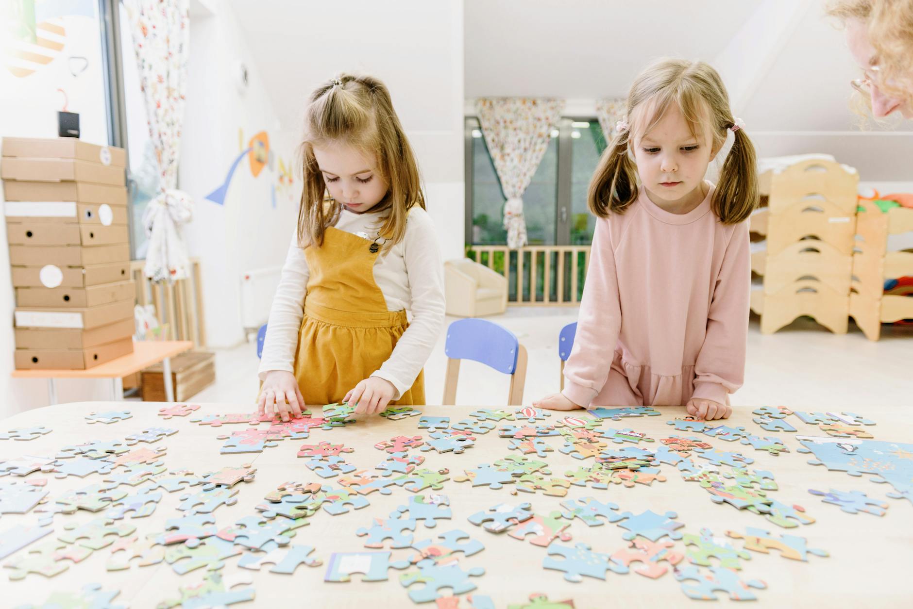 Two young girls solving puzzles at a kindergarten table with focus and creativity. - preschool sharing activities