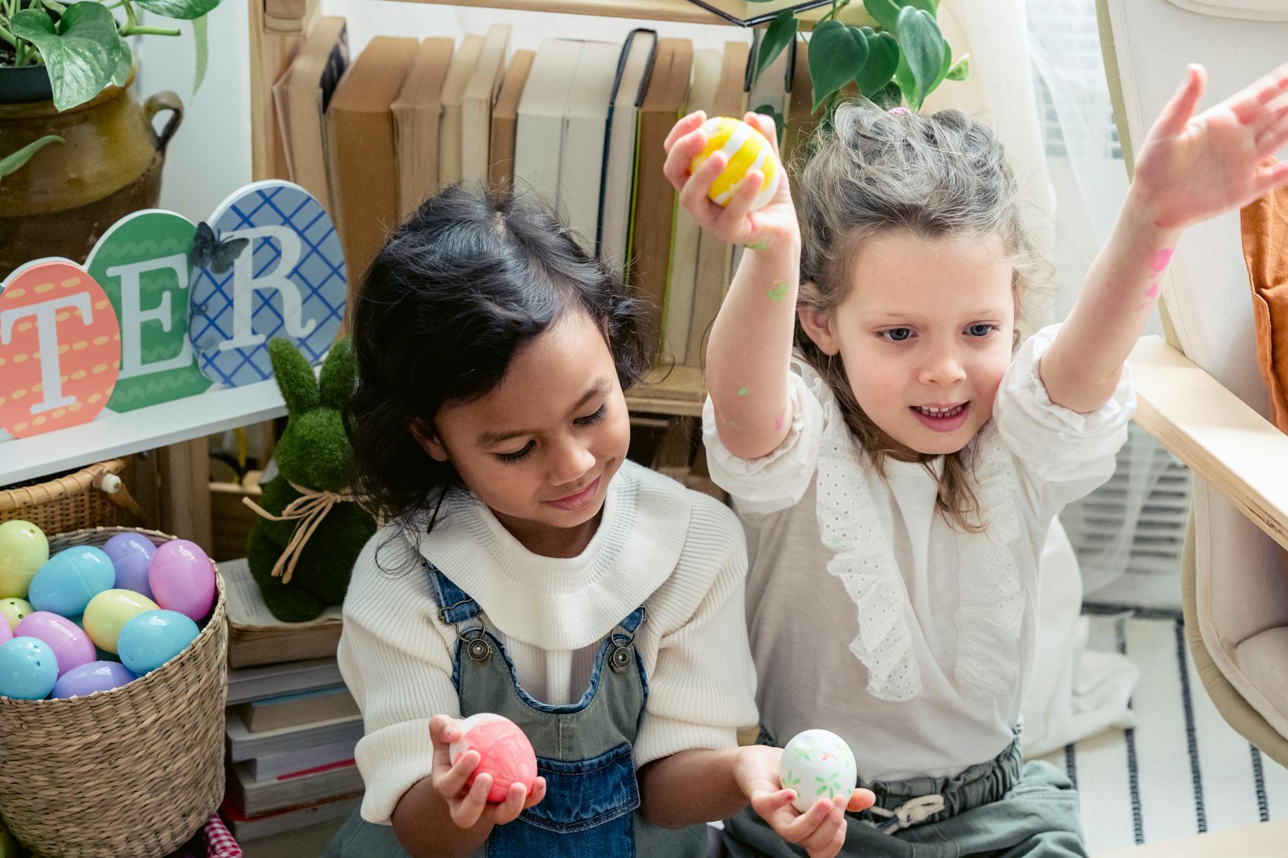 Cheerful diverse children with painted eggs sitting in light room with creative decoration during festive Easter holiday celebration at home - preschool spring crafts
