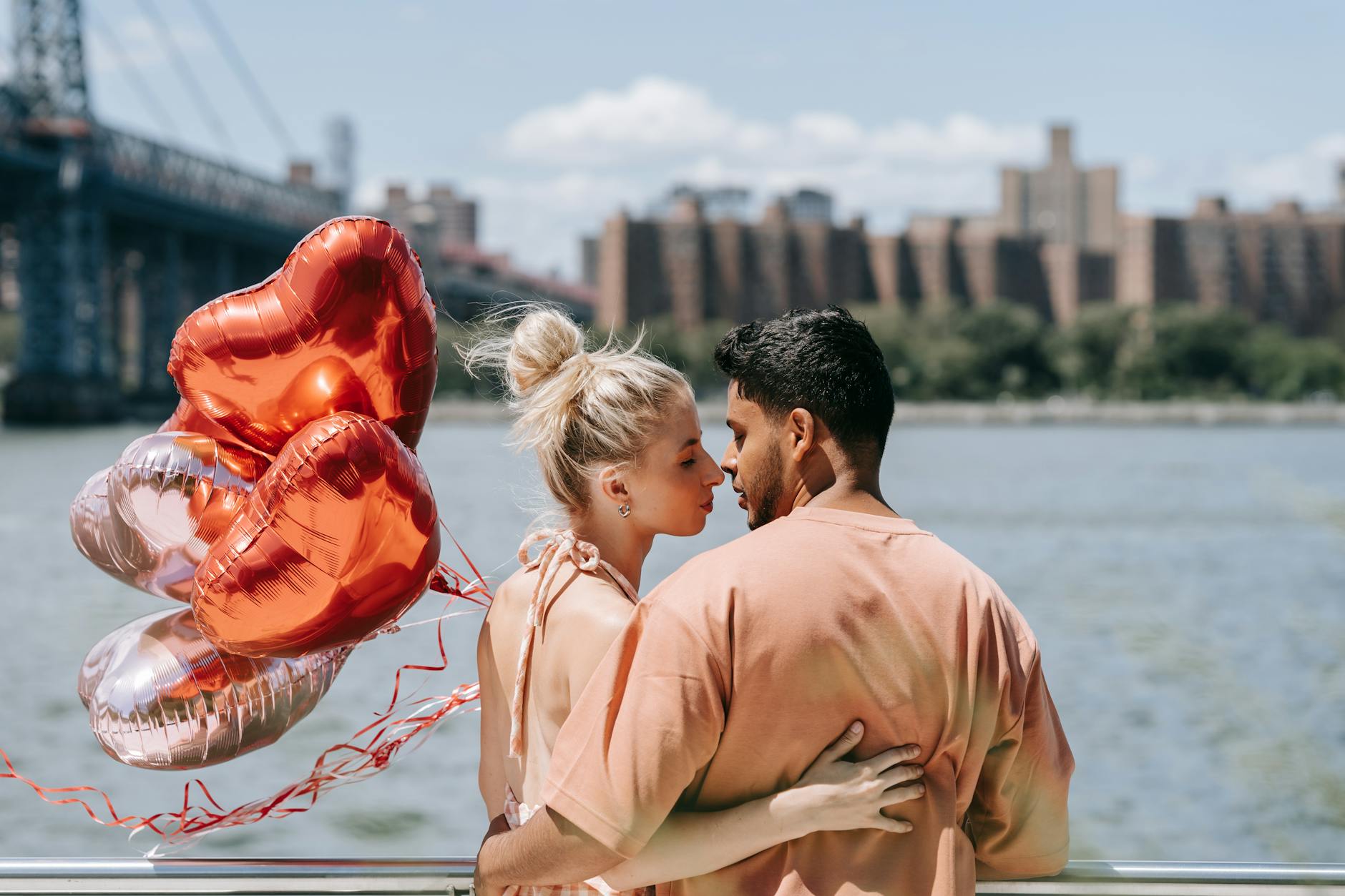 An interracial couple embracing by the water, holding heart-shaped balloons on a sunny day. - rekindle relationship passion