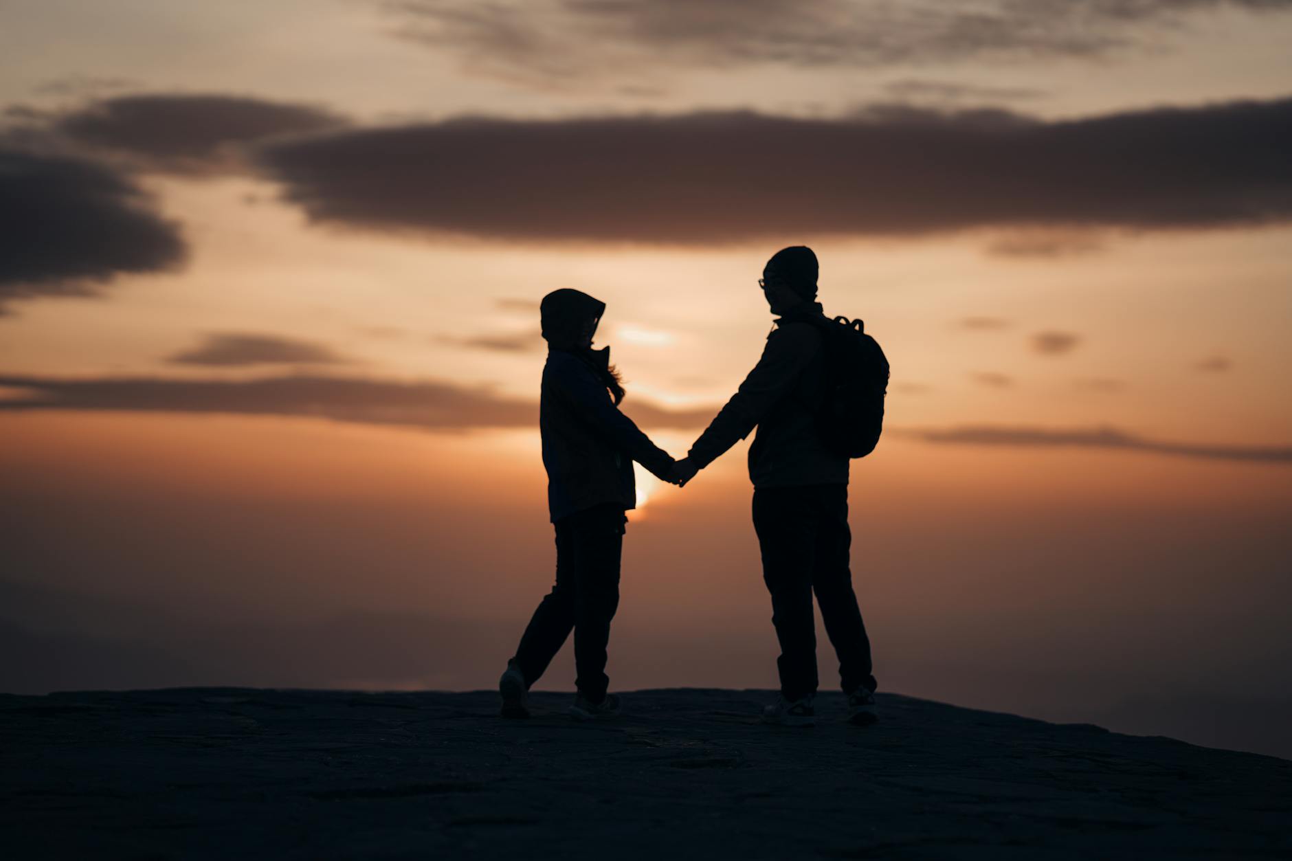 Silhouette of a couple holding hands against a dramatic sunset sky. - relationship check in