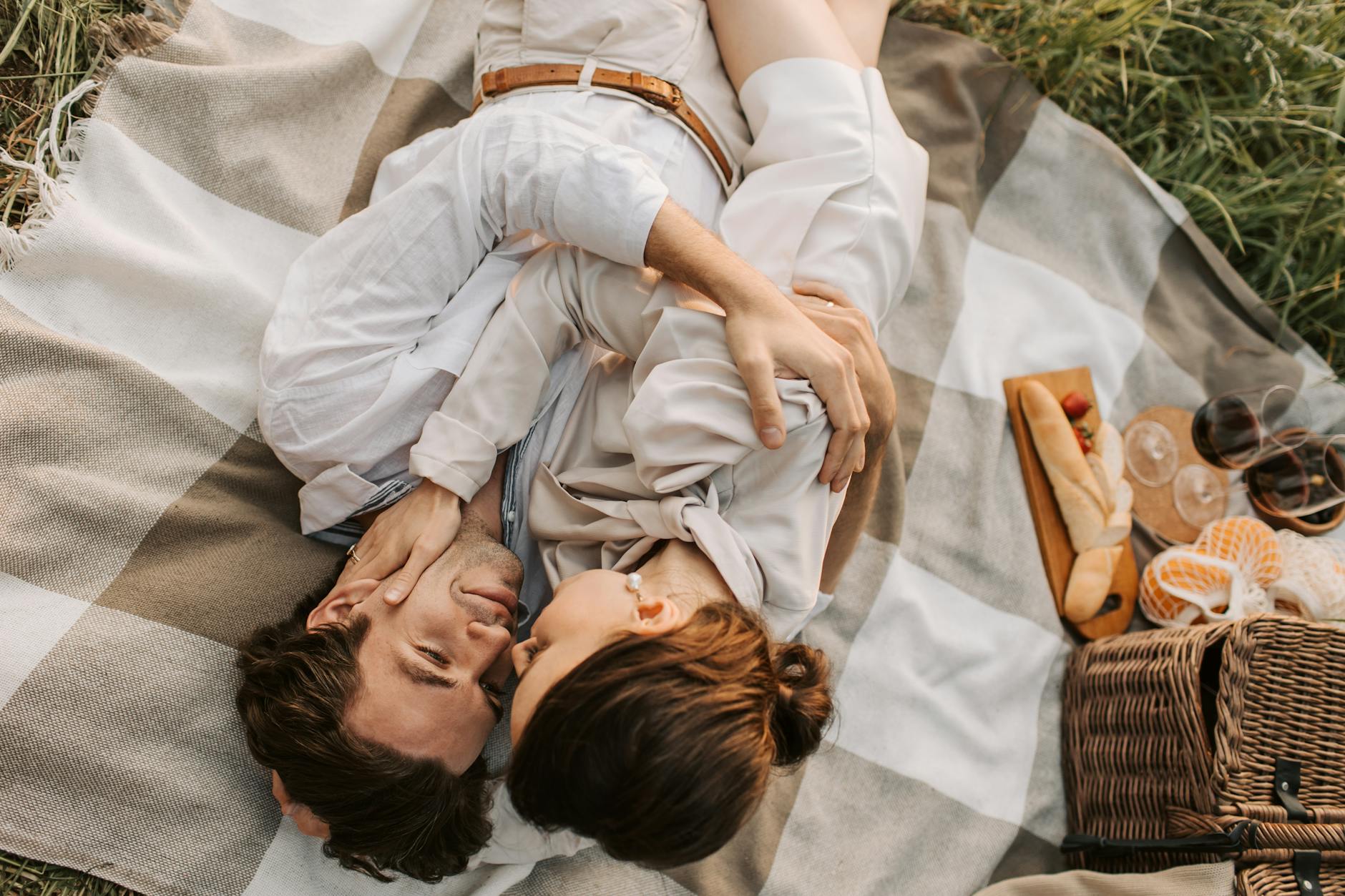A couple shares a tender moment during a picnic on a checkered blanket in a grassy field. - relationship renewal ideas