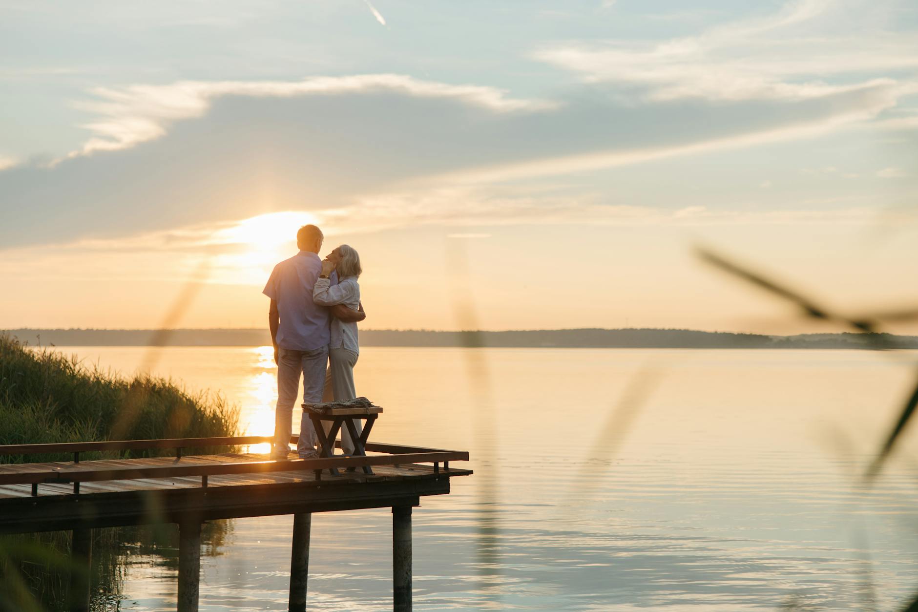 A senior couple embraces on a wooden dock at sunset, exuding tranquility and affection. - relationship renewal ideas