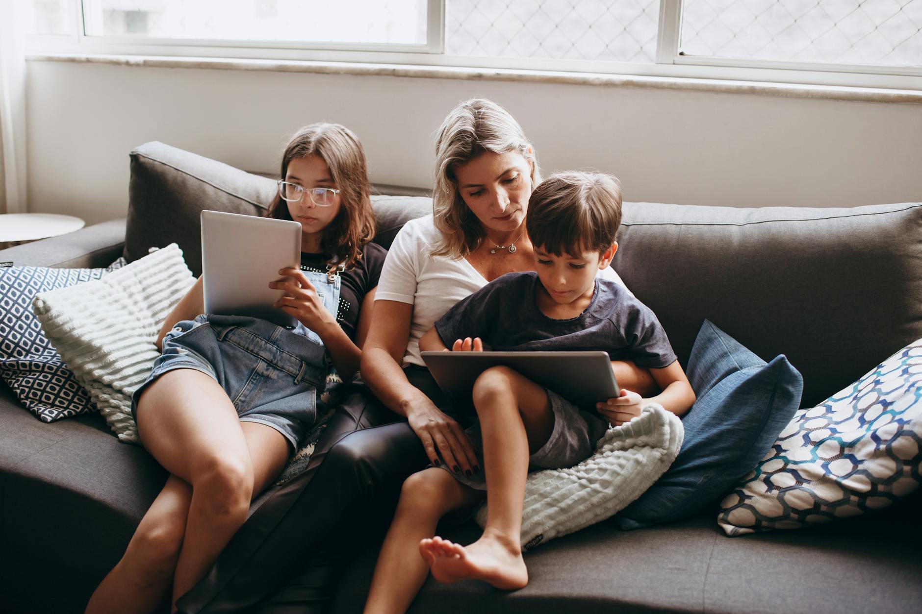 A family enjoying leisure time indoors, using tablets together on a sofa. - screen time limits