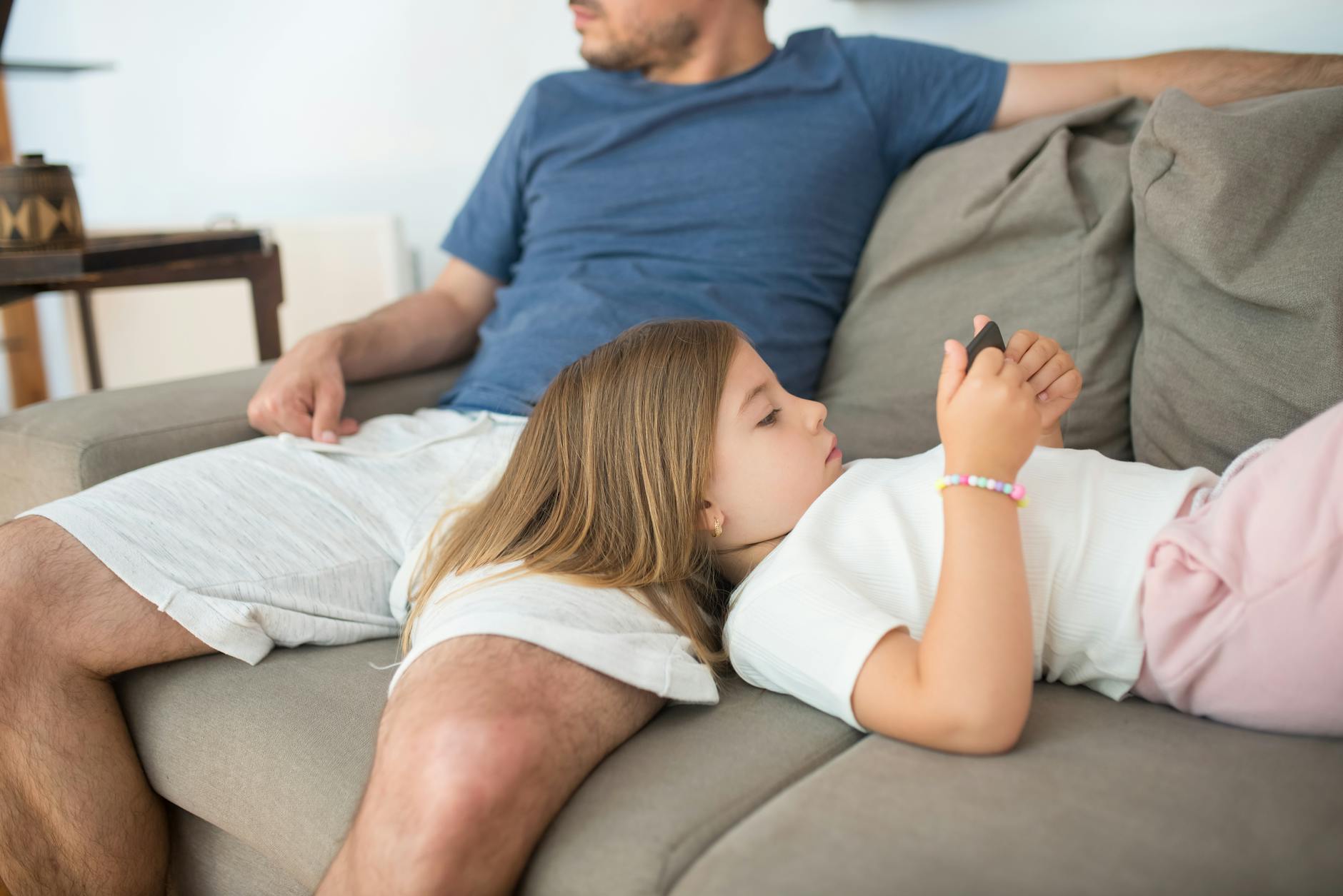 A father and daughter enjoying a relaxing day indoors, with the daughter watching something on a smartphone. - screen time limits