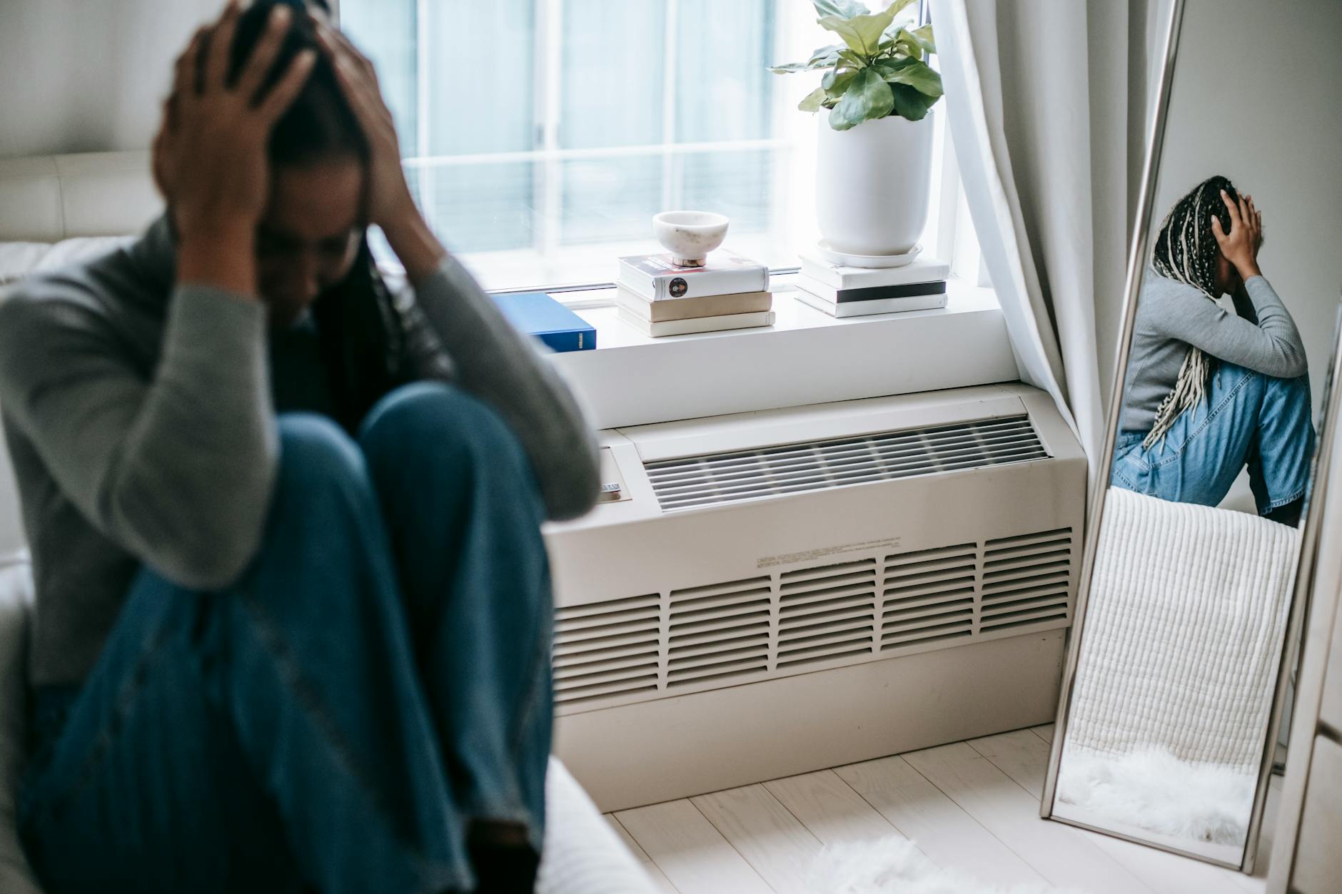 Frustrated young female having mental problem reflecting in mirror while sitting alone in room - seasonal depression treatment