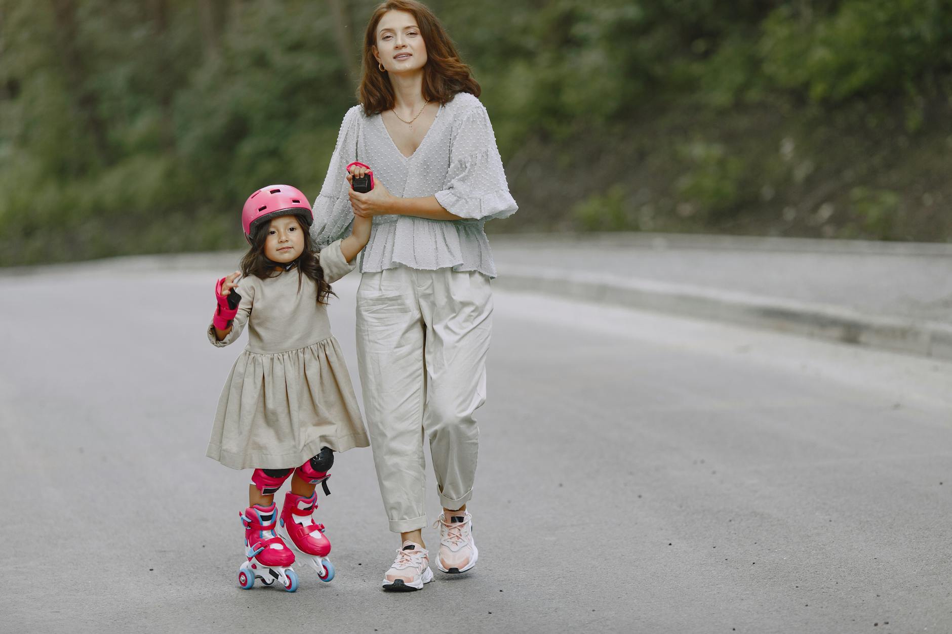 Mother holding daughter's hand while teaching her to rollerblade on a scenic road. - spring outdoor safety