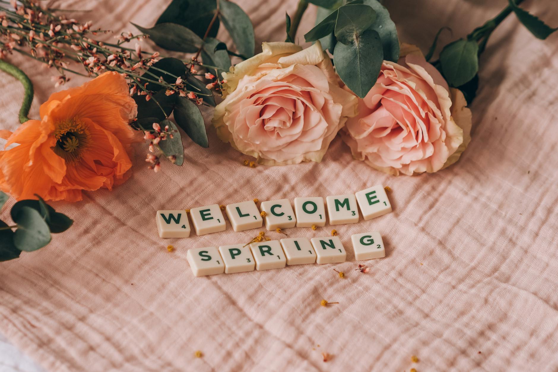 A beautiful floral arrangement on fabric with Scrabble tiles spelling "Welcome Spring." - spring slump therapy