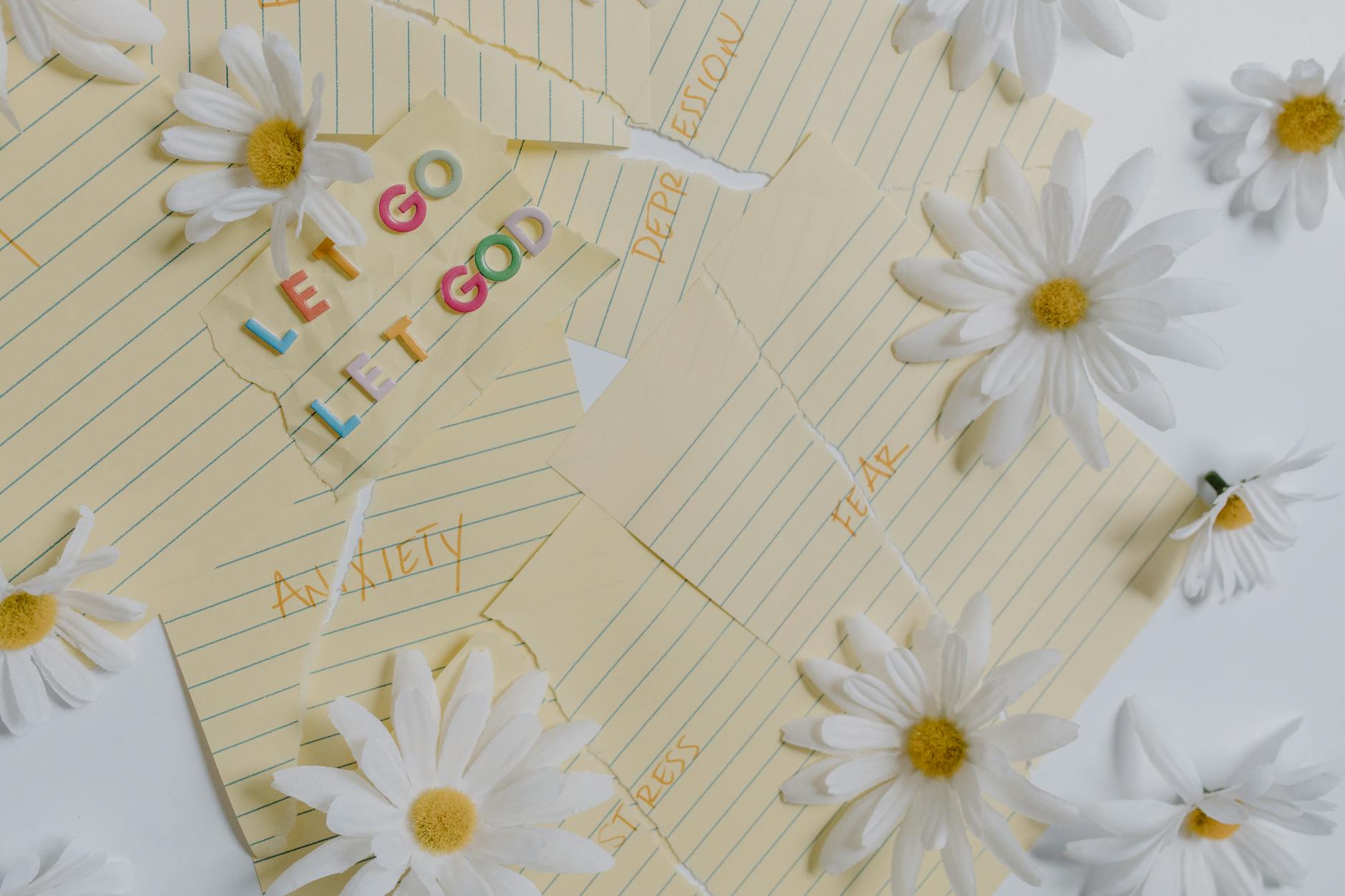 Flat lay of daisies and motivational notes with phrases like 'Let Go Let God' on a white background. - spring stress management