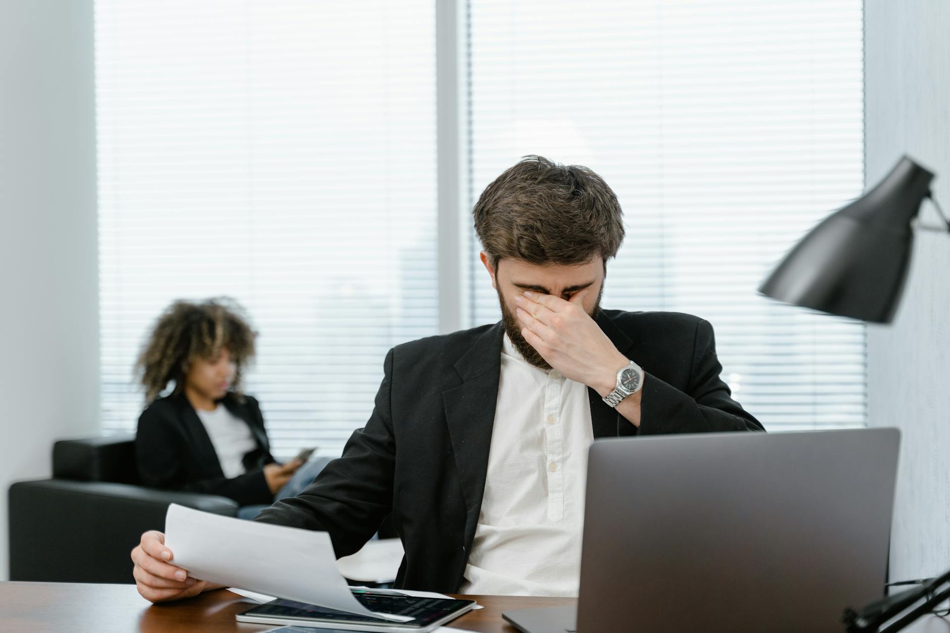 Businessman in an office covering his eyes while working on a laptop, feeling stressed. - spring stress management