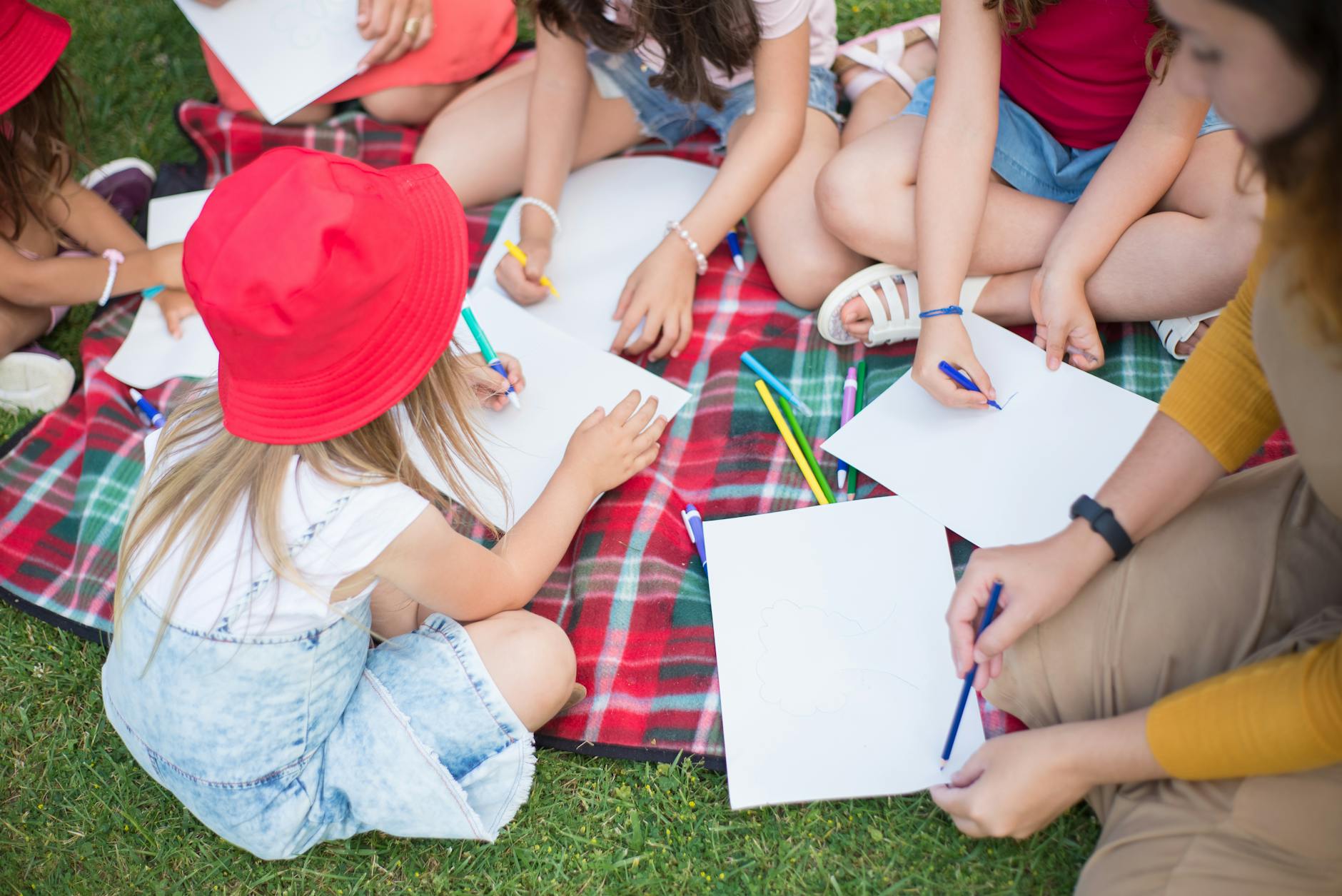 A group of children creatively drawing together on paper outdoors on a picnic blanket. - summer learning activities