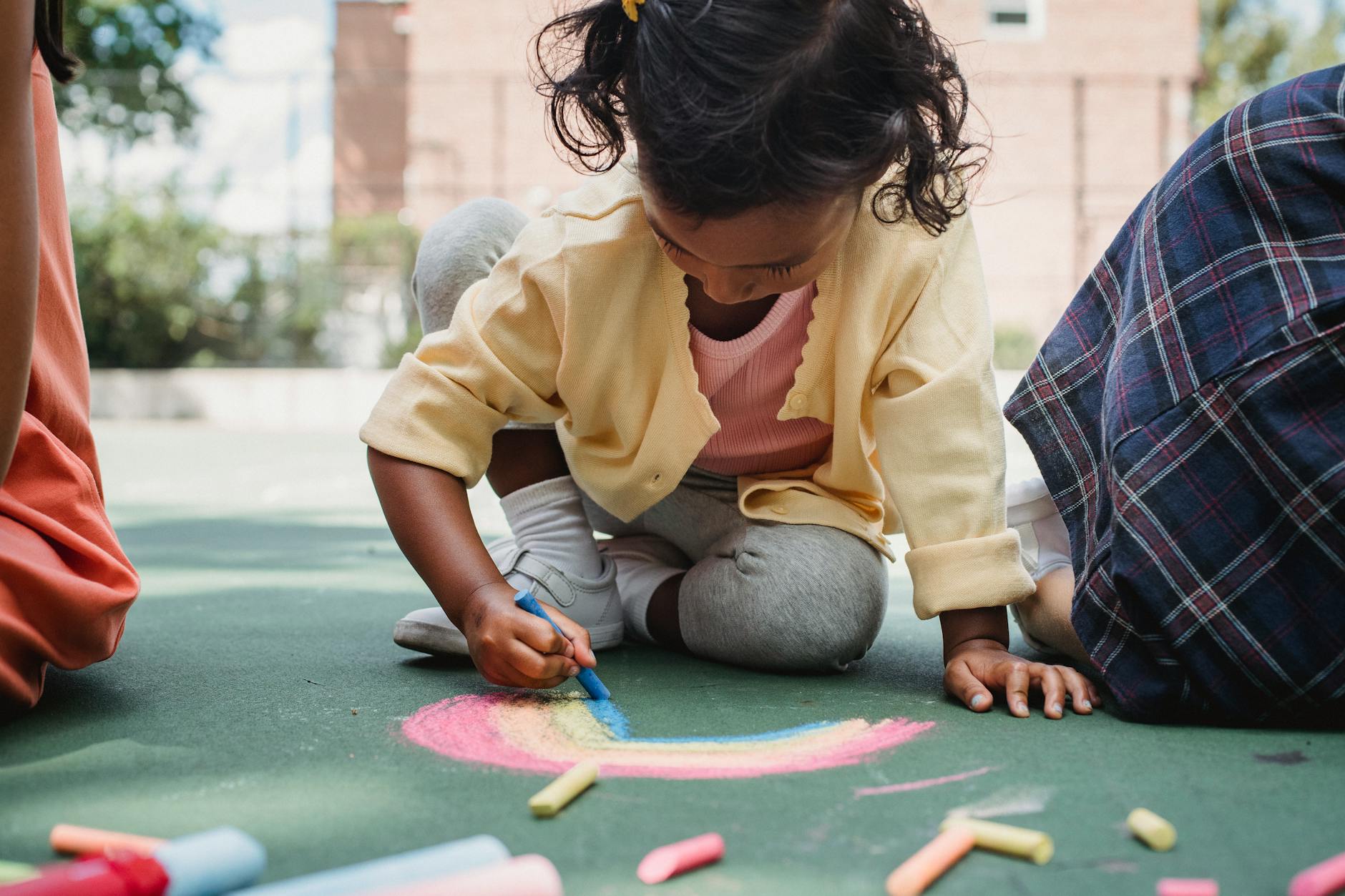 A young child enjoying creative play with chalk on a sunny outdoor playground. - summer learning activities