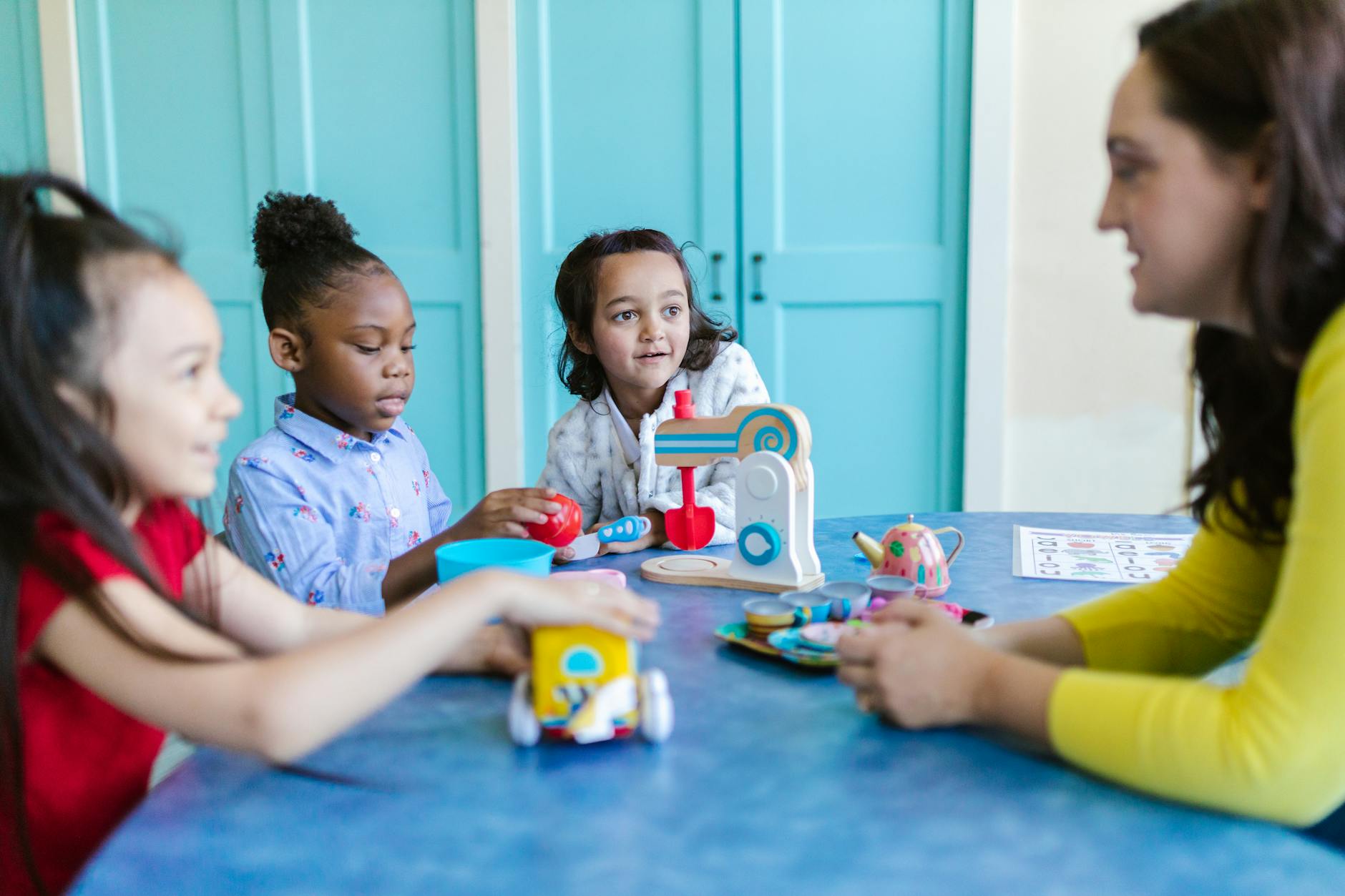Young children engaged in play with toys and a teacher in a colorful preschool setting. - teach empathy preschoolers