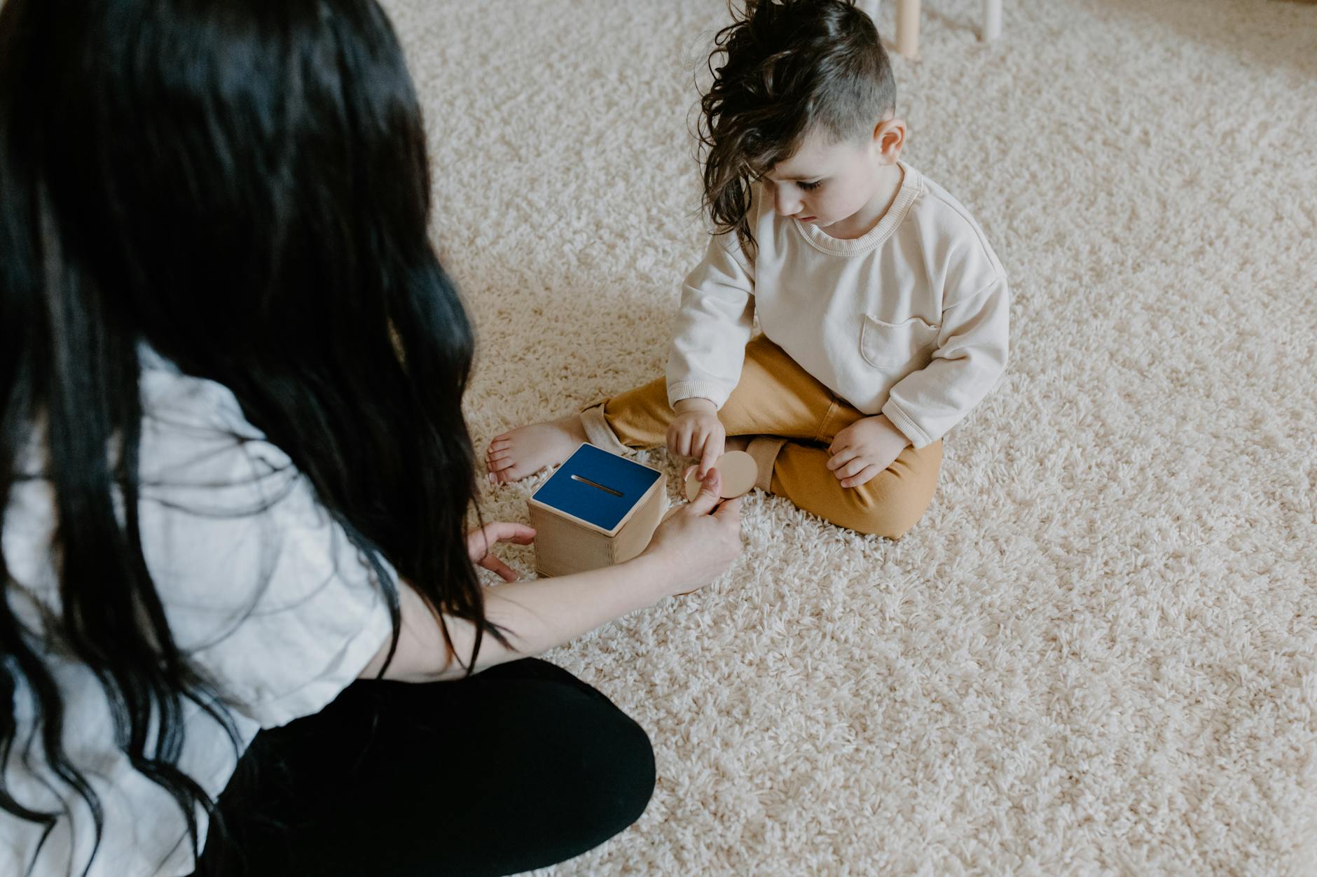 A young child playing with an educational wooden toy on a soft carpet indoors. - teaching toddlers sharing