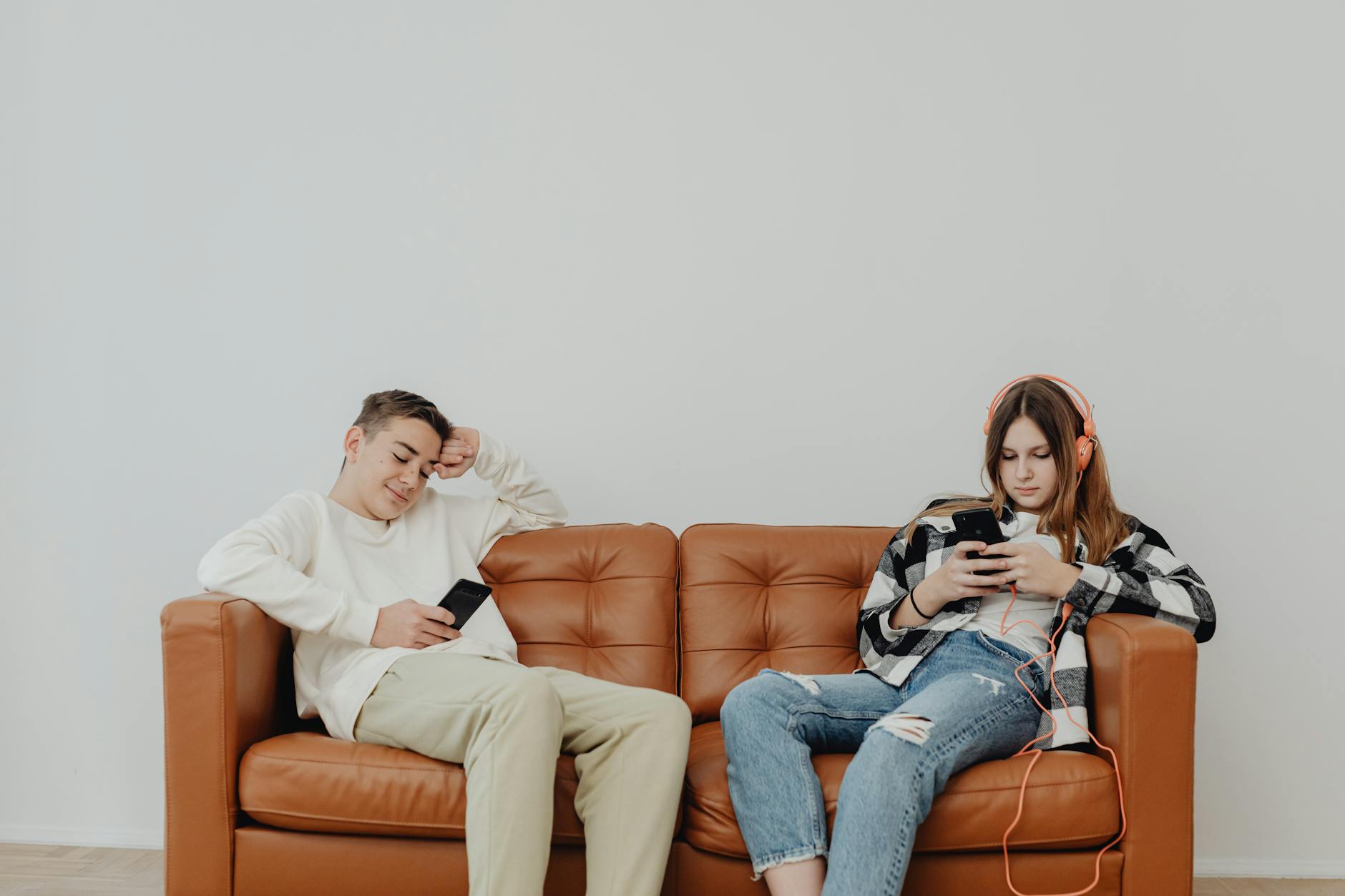 Teenagers lounging on a leather sofa using smartphones, displaying modern leisure. - teen social pressure