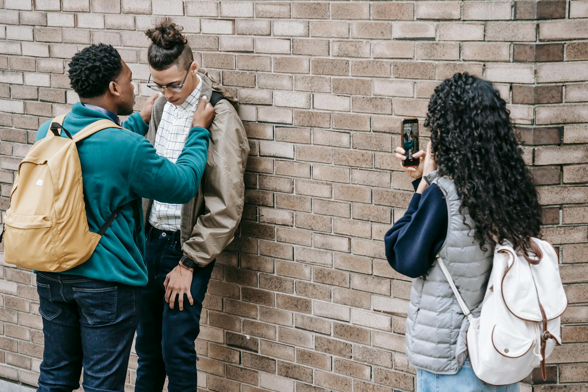 Back view of classmates grabbing student while filming video on smartphone in yard - teen social pressure