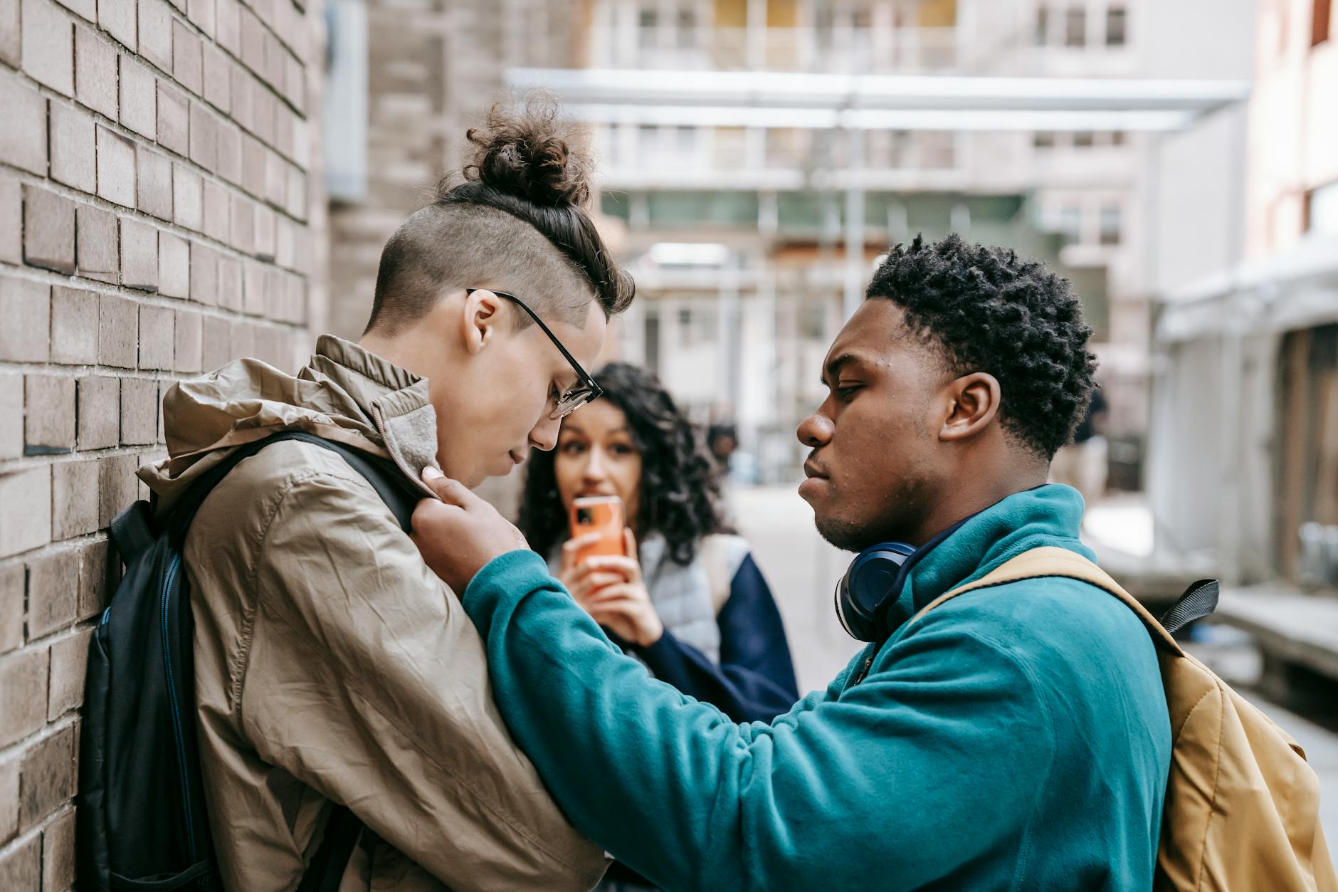 Side view of multiracial classmates bullying student near brick wall and filming video on smartphone - teen social pressure