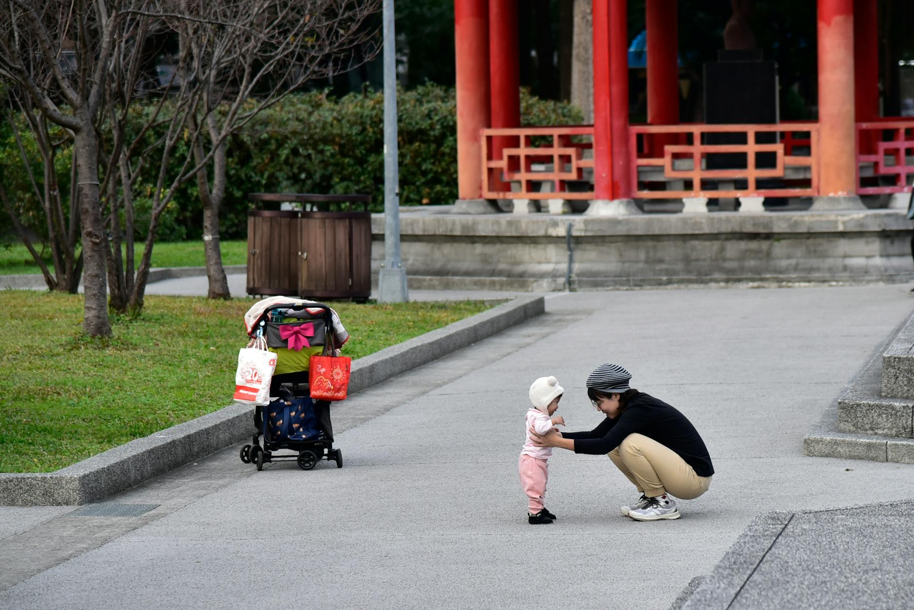 A mother helps her baby stand near a colorful pavilion in a park setting. - toddler personal space