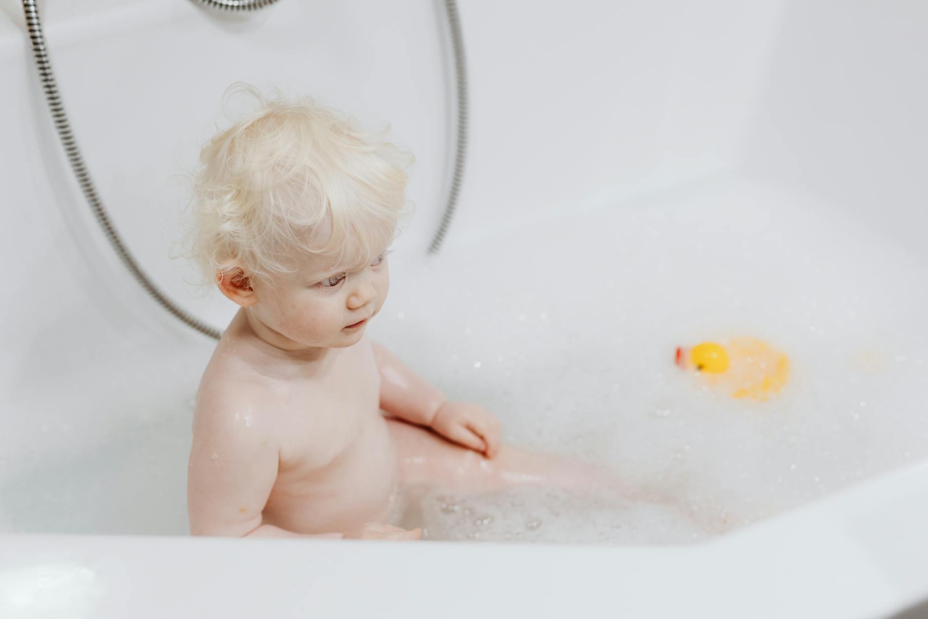 Cute blonde baby enjoying a bubble bath with a rubber duck. Perfect for hygiene and childhood concepts. - toddler self care
