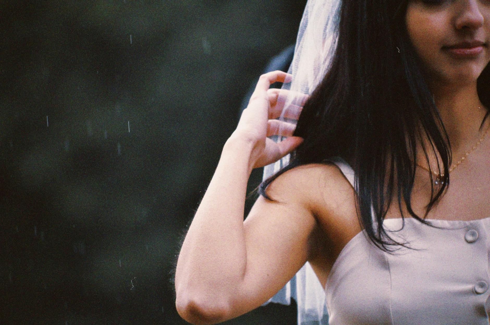 Bride in a wedding dress adjusting her veil on a rainy day outdoors. - wedding day anxiety
